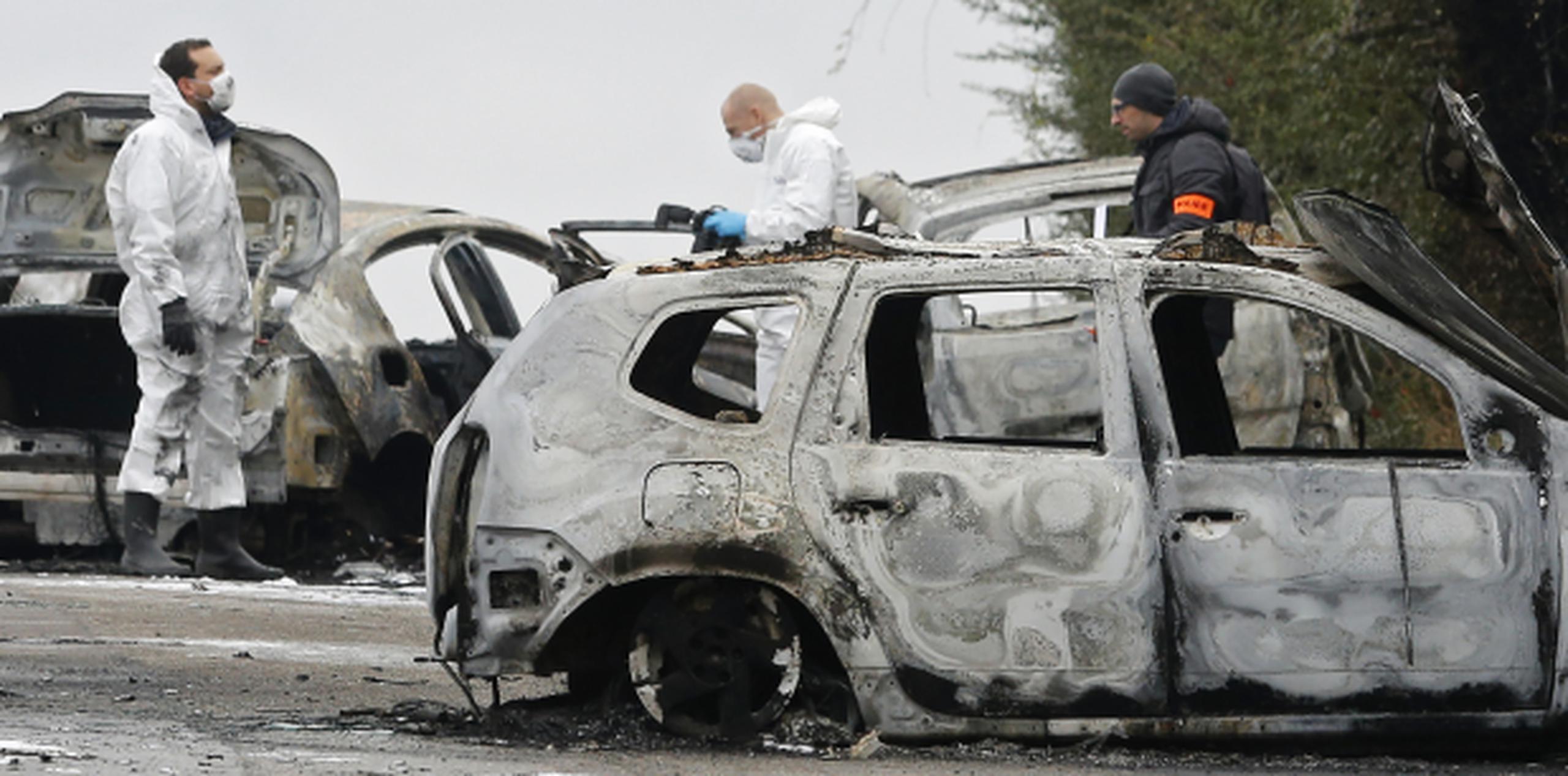 Policías inspeccionan los autos incendiados como parte de su investigación al robo del camión en París. (AP)