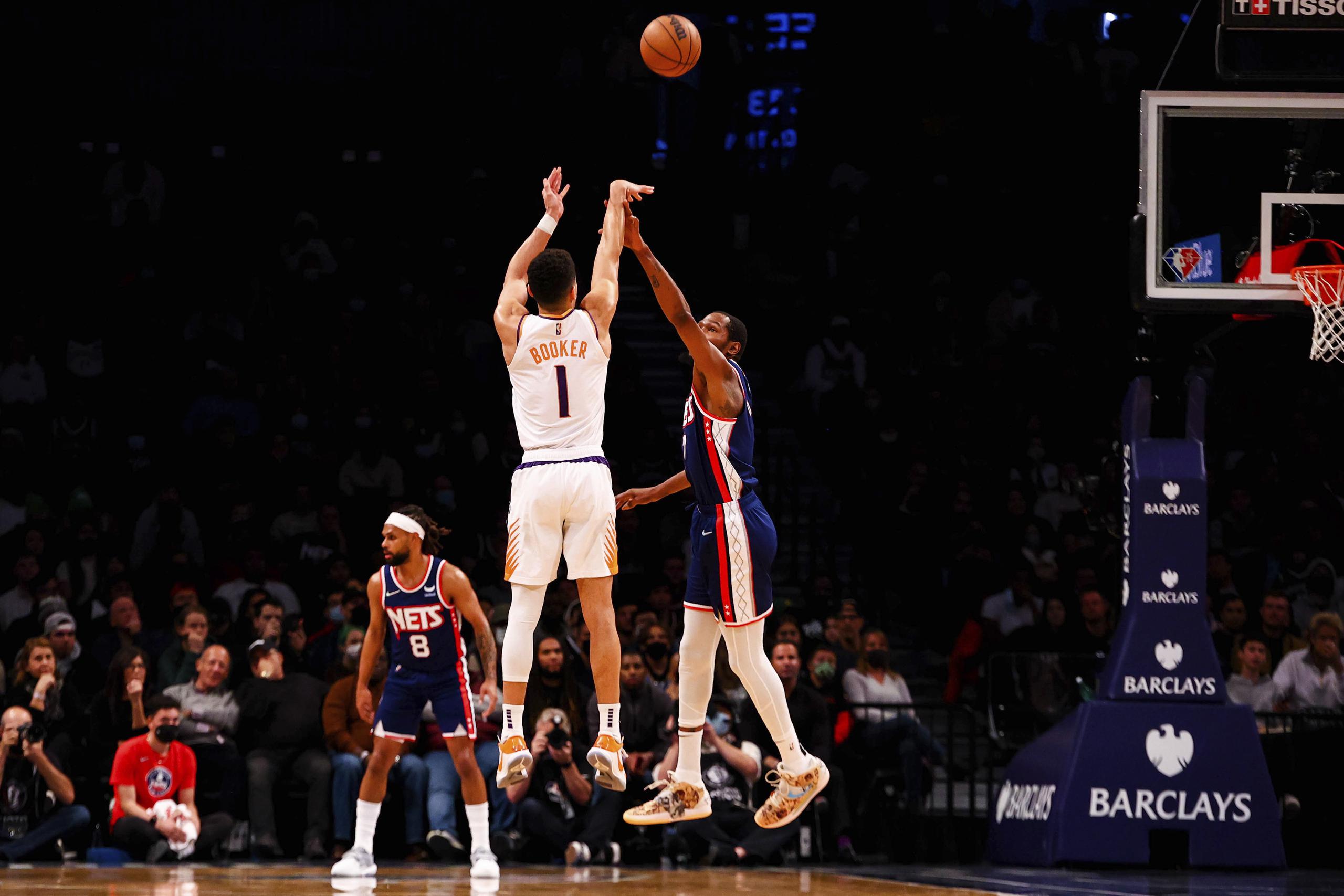 El defensa de los Suns de Phoenix, Devin Booker (3), realiza un disparo por encima de la defensa de Kevin Durant, de los Nets de Brooklyn, durante el partido del sábado que los Suns dominaron 113-107.