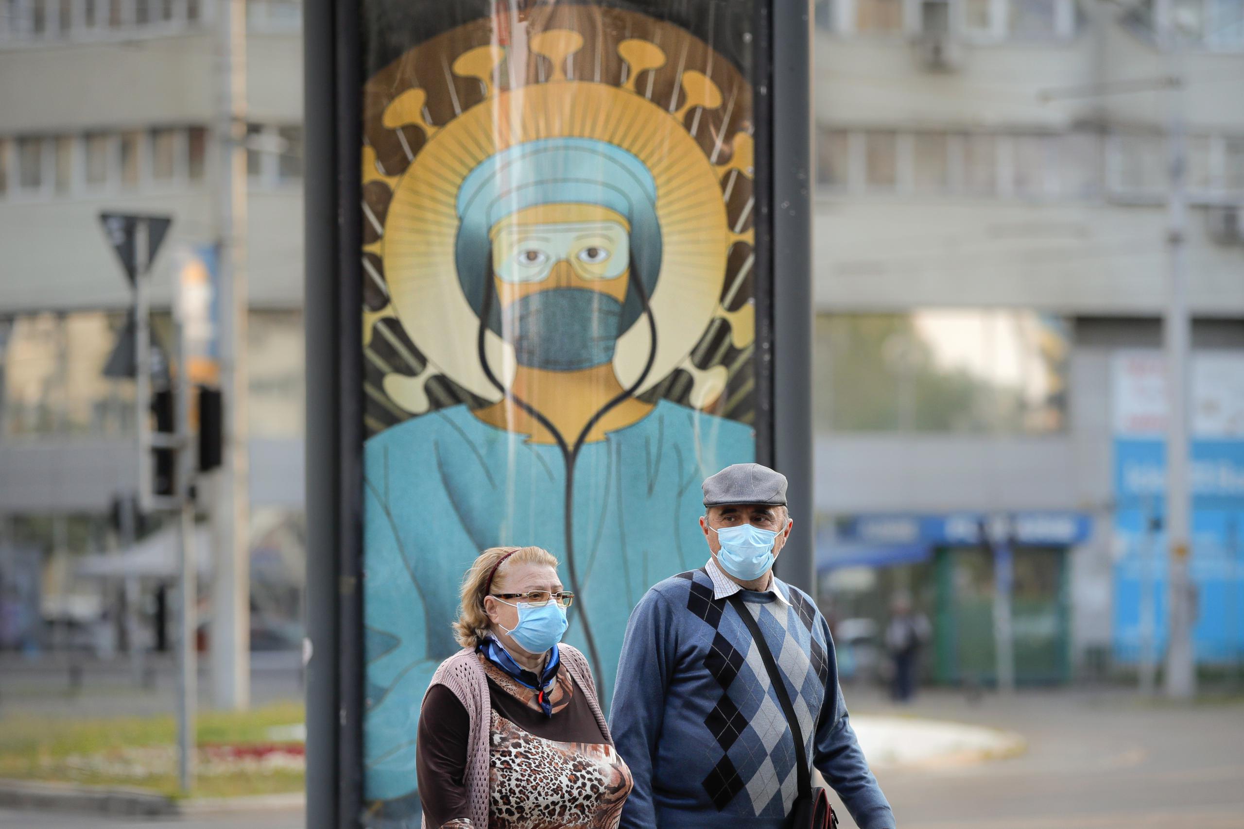 Ancianos con mascarillas pasan frente a una pintura de un empleado médico con equipo protector al estilo del Cristo Pantocrátor en Bucarest, Rumania