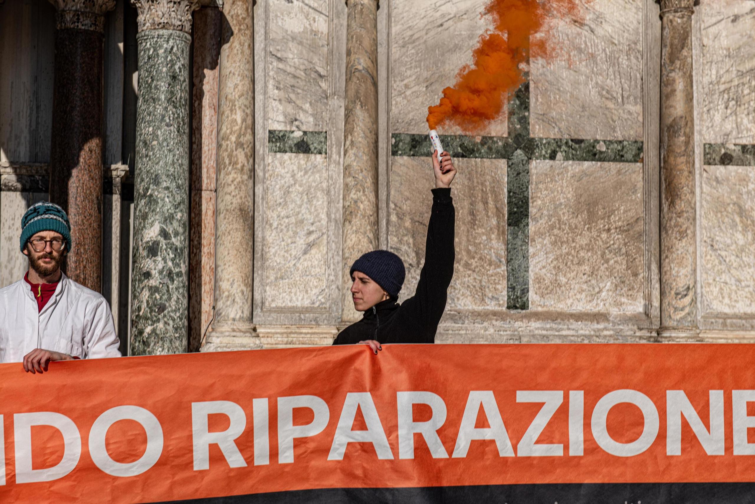 Activistas climáticos sostienen una pancarta después de rociar barro en el exterior de la Basílica de San Marcos durante una protesta en Venecia, Italia, el 7 de diciembre de 2023. Los manifestantes utilizaron extintores para rociar barro líquido en la iglesia paredes, antes de desplegar una pancarta que decía "fondo de reparación". (Protestas, Italia, Niza, Venecia) (EFE/EPA/EDOARDO FIORETTO)