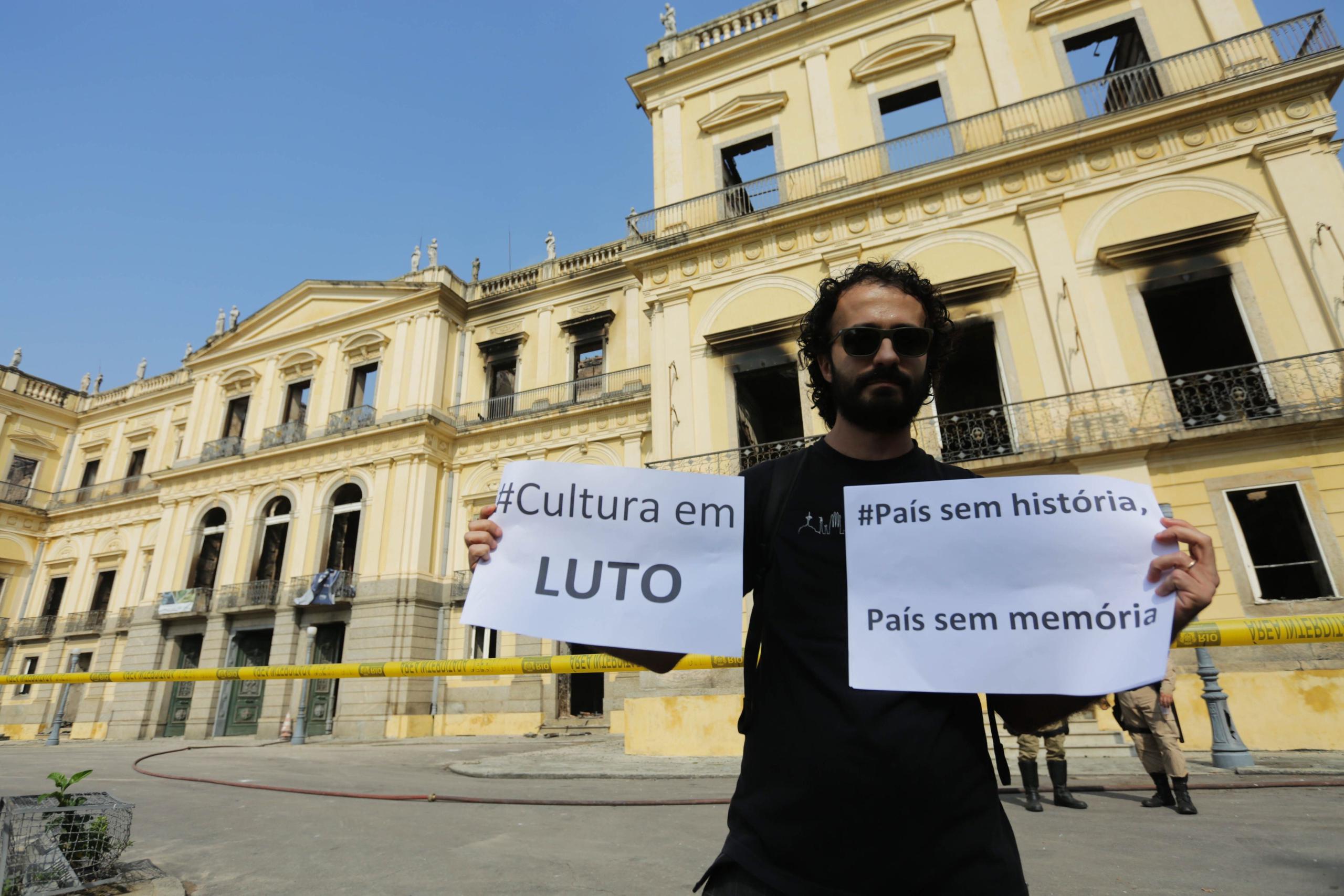 Un hombre muestra un cartel en el que se lee "Cultura en luto" frente al museo. (EFE / Antonio Lacerda)