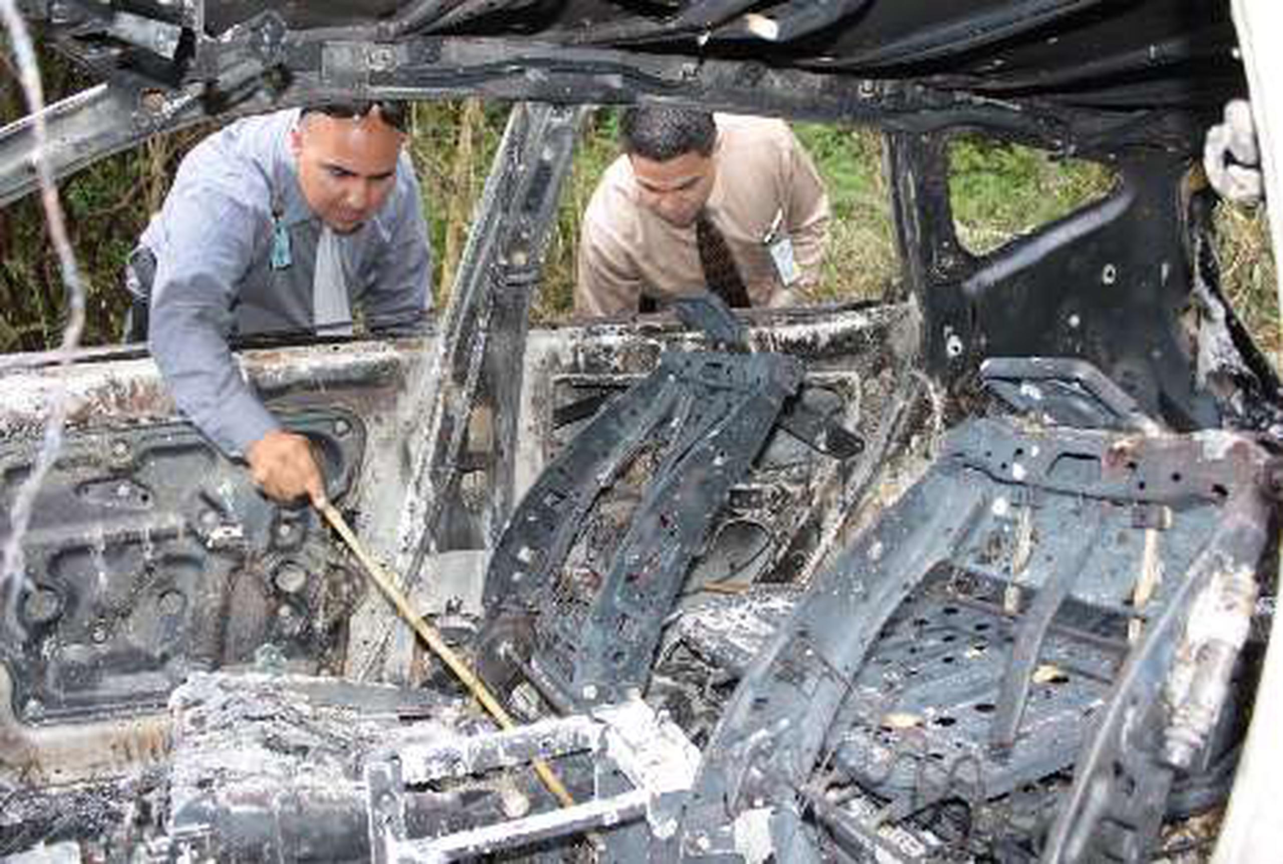  Agentes del CIC de Arecibo inspeccionan un vehículo quemado a la orilla de la carretera PR-673 el que está vinculado  aparentemente con el asesinato de Rosado Santana.