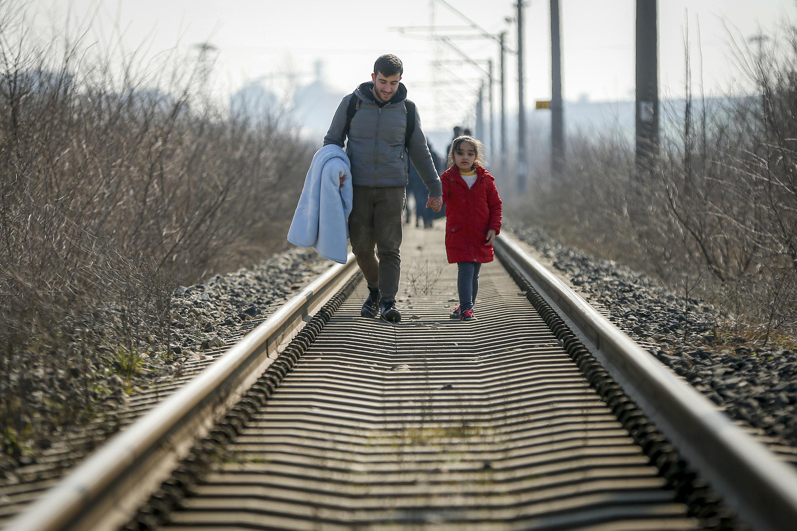 Una niña y un adulto caminan por los rieles de un tren desde Turquía a Grecia.