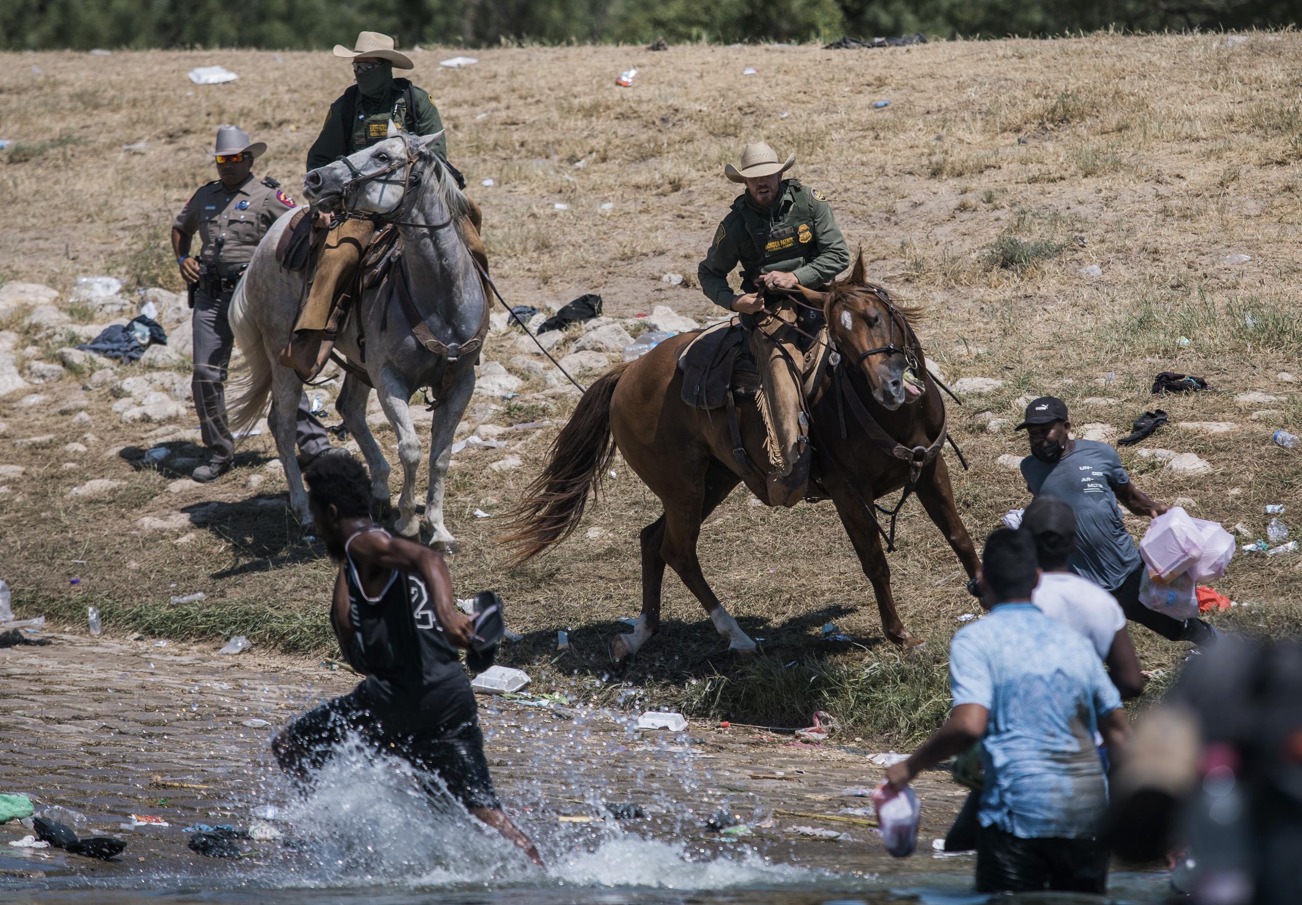 Oficiales a caballo del Servicio de Fronteras y Aduana intentan contener a los migrantes haitianos para que no crucesn de Ciudad Acuña en México hacia Del Río, Texas.