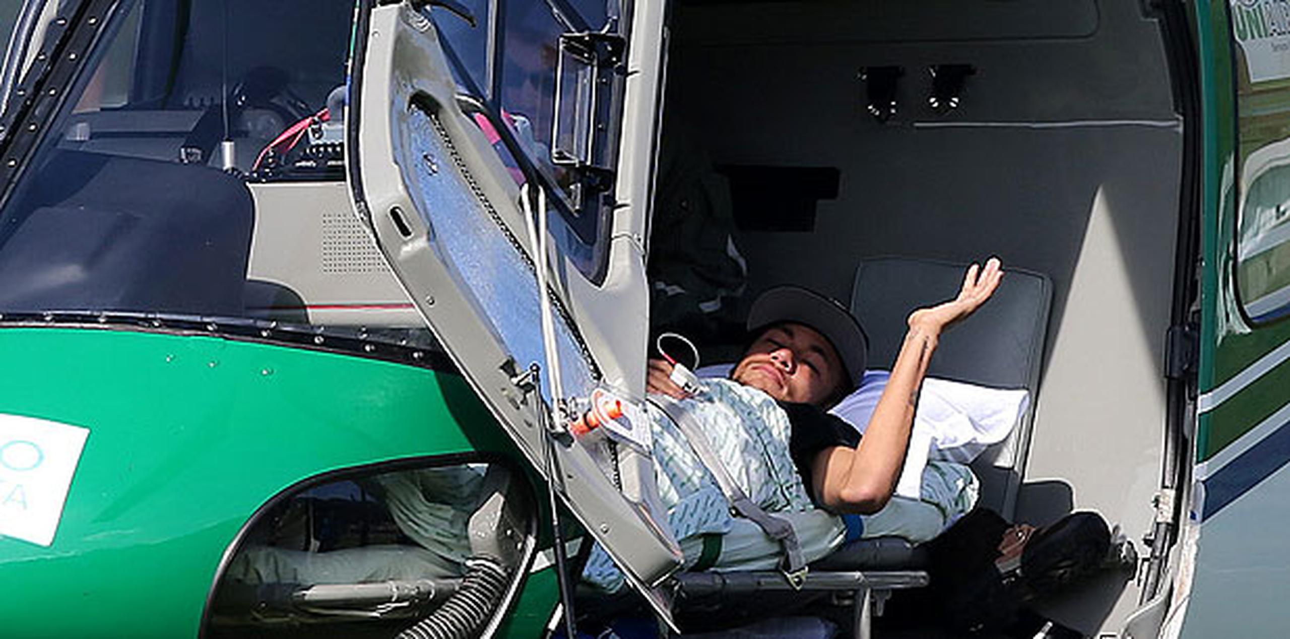 Los canales de información deportiva transmitieron en directo la imagen de Neymar, quien levantó una mayo para saludar desde la camilla en el helicóptero. (EFE)