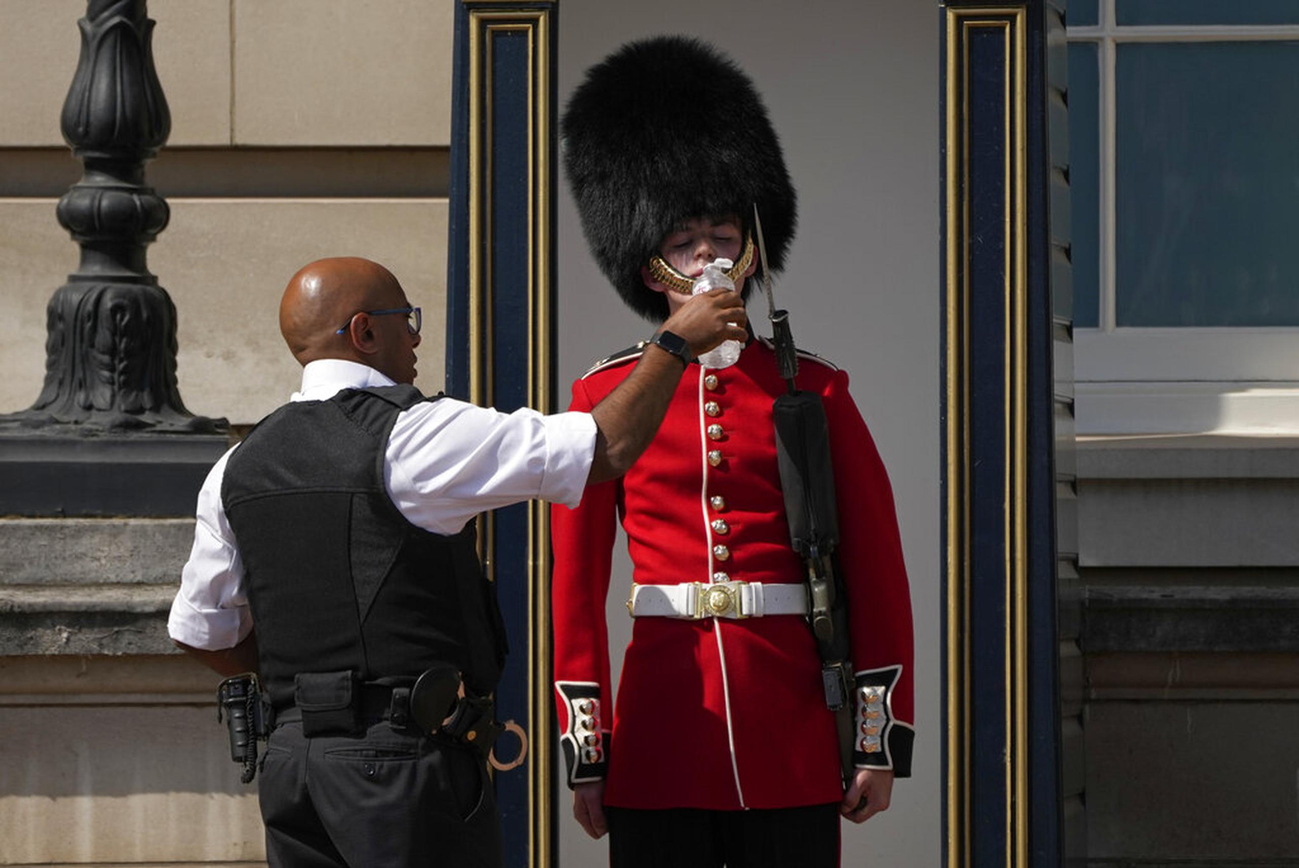 Un policía le da agua a un soldado británico frente al Palacio de Buckingham en Londres el 18 de julio de 2022.