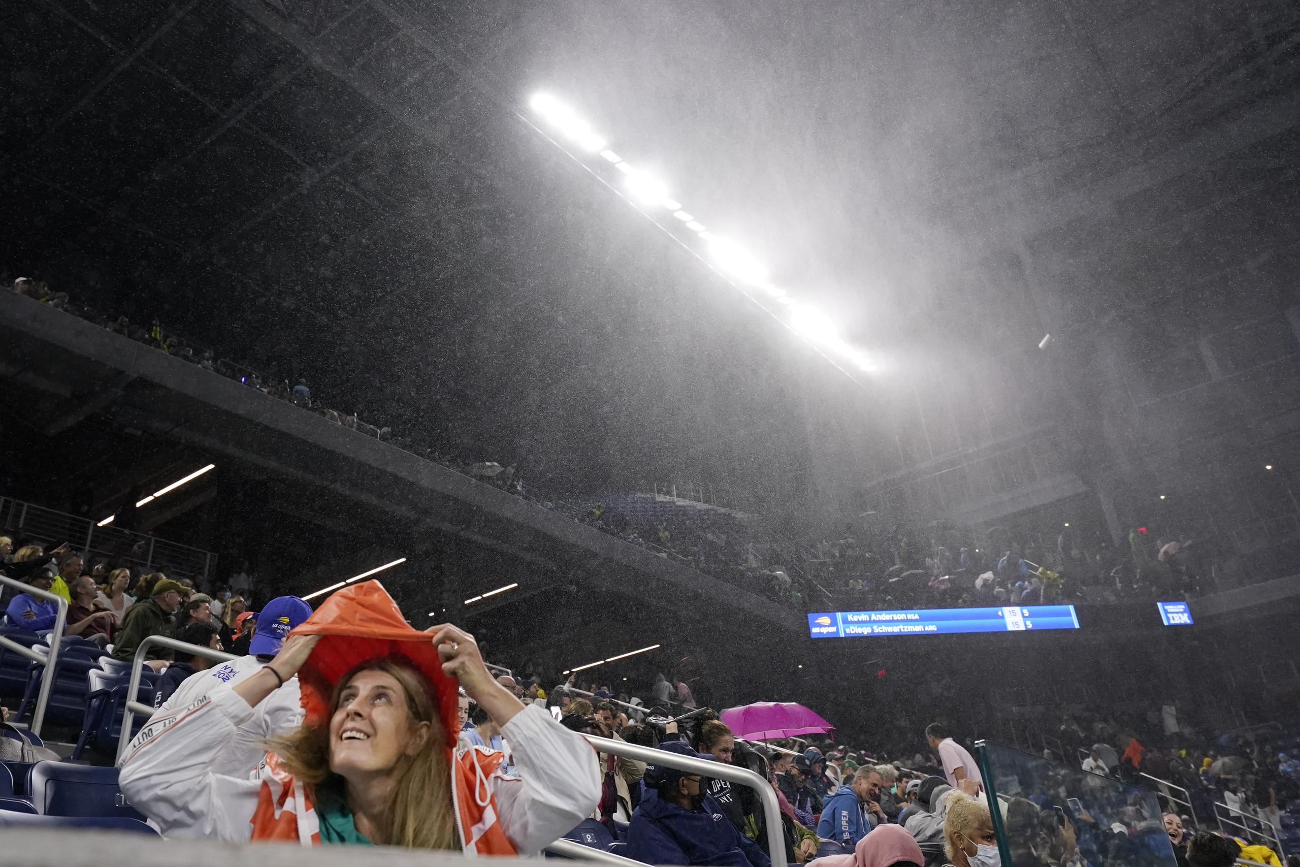 Una aficionado se cubre de la lluvia en el estadio Louis Armstrong durante el partido entre 
Kevin Anderson y Diego Schwartzman por la segunda ronda del Abierto de Estados Unidos, el miércoles 1 de septiembre de 2021, en Nueva York. (AP Foto/Frank Franklin II)