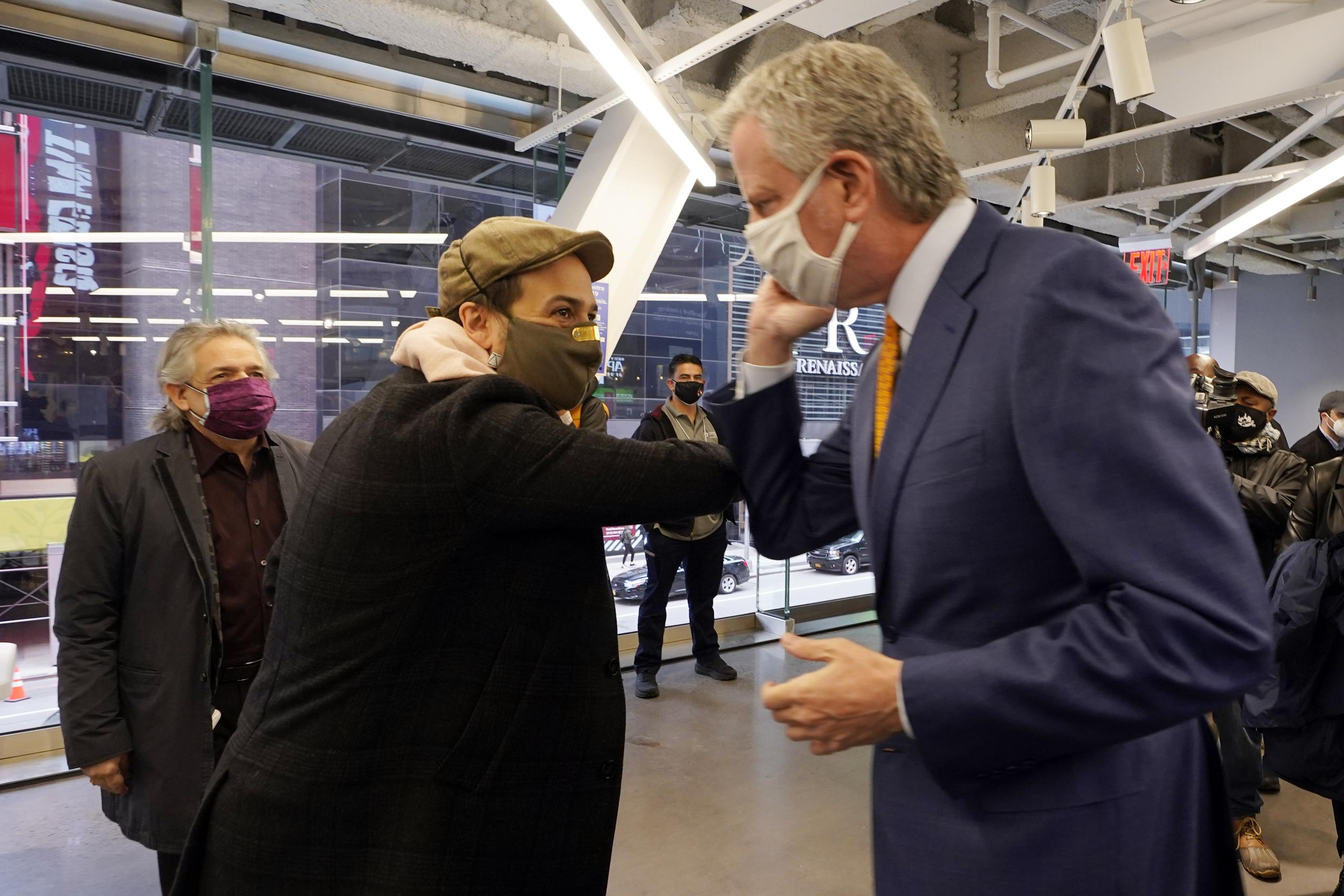 El actor Lin-Manuel Miranda, centro, y el alcalde de Nueva York Bill de Blasio se saludan con los codos antes de hacer un recorrido en la inauguración del centro de vacunación.