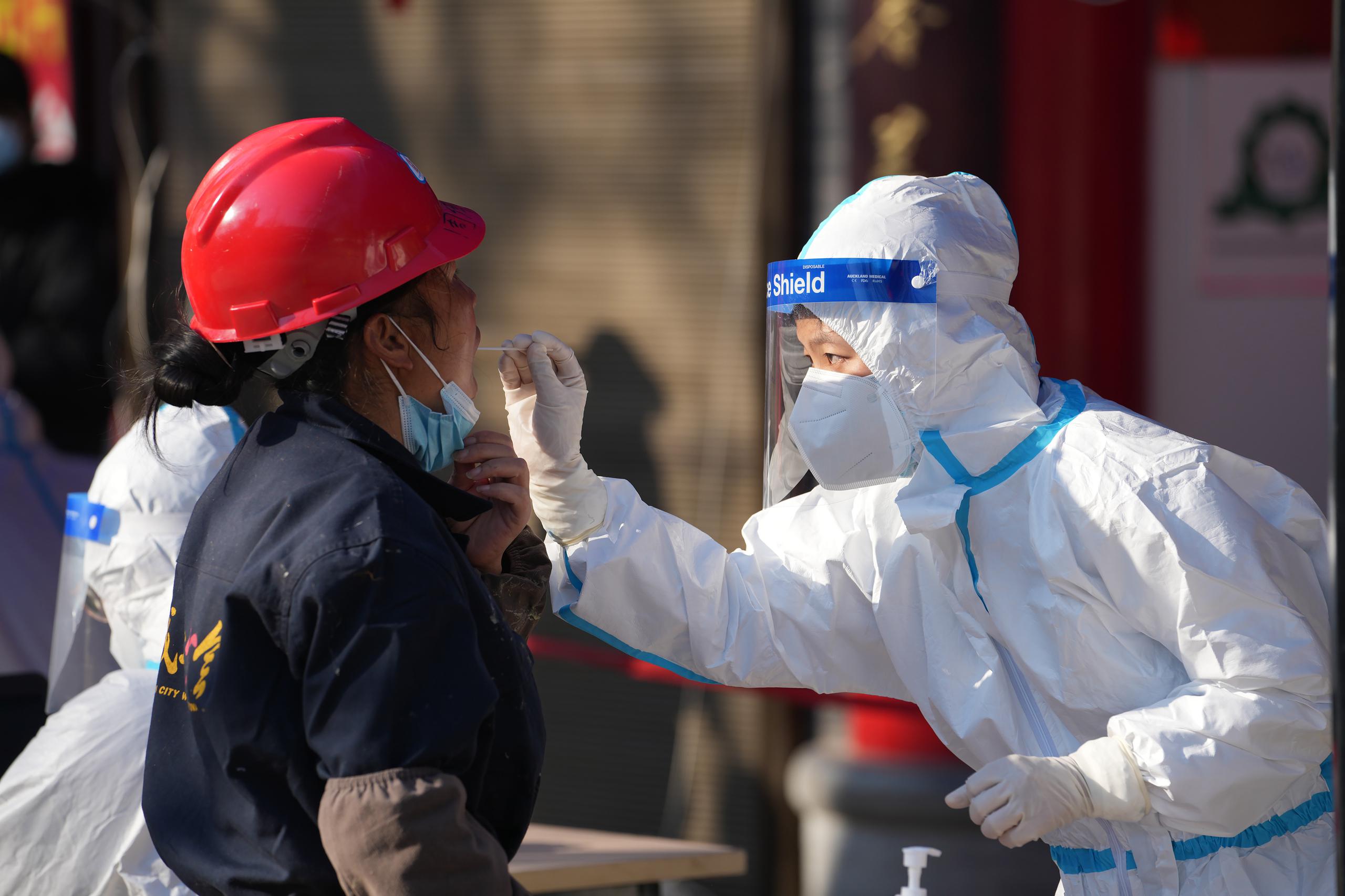 En esta fotografía publicada por la agencia de noticias china Xinhua, un trabajador toma una muestra en un sitio de pruebas de coronavirus, en Xi'an, en China, el martes 21 de diciembre de 2021. (Li Yibo/Xinhua vía AP)