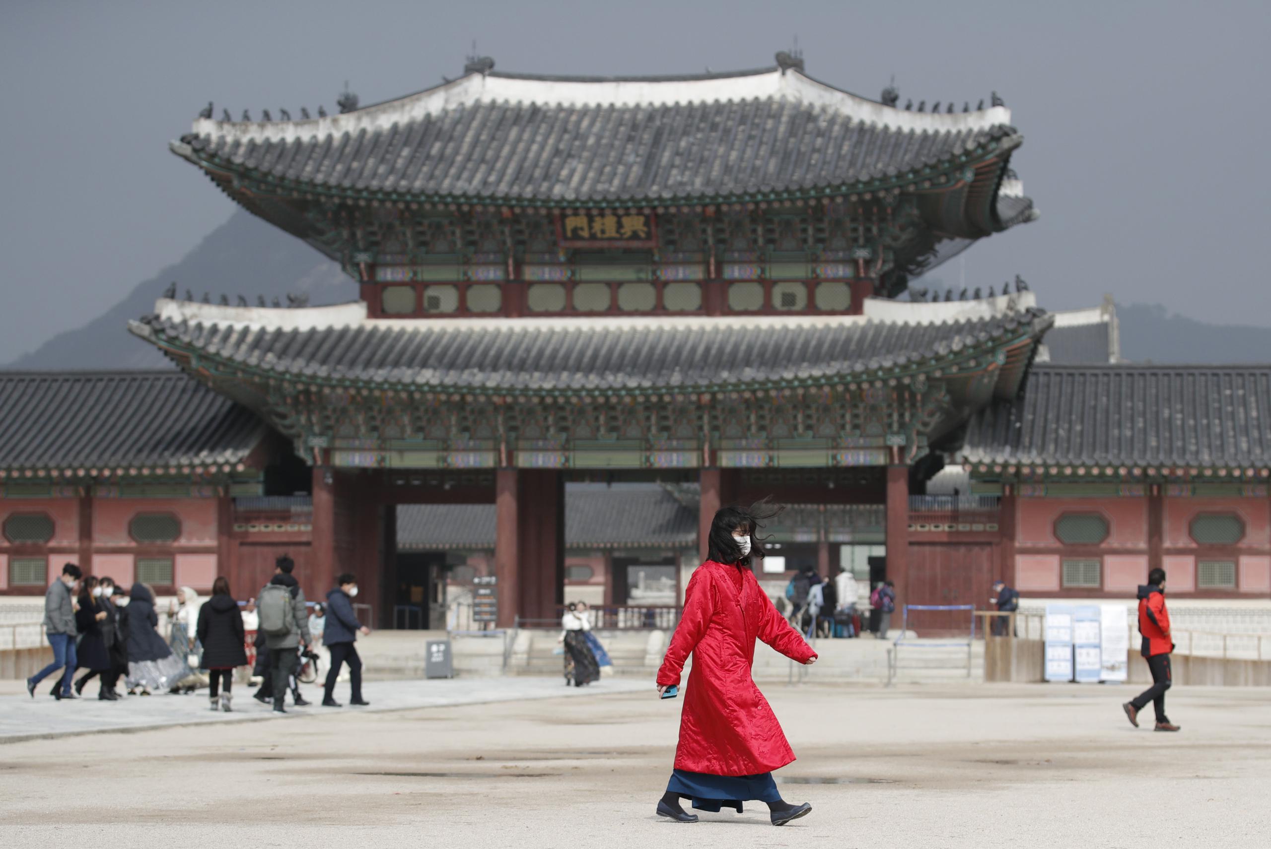 Una mujer con la boca cubierta por una mascarilla camina por delante del Palacio Gyeongbok, uno de los monumentos más conocidos de Corea del Sur, en Seúl