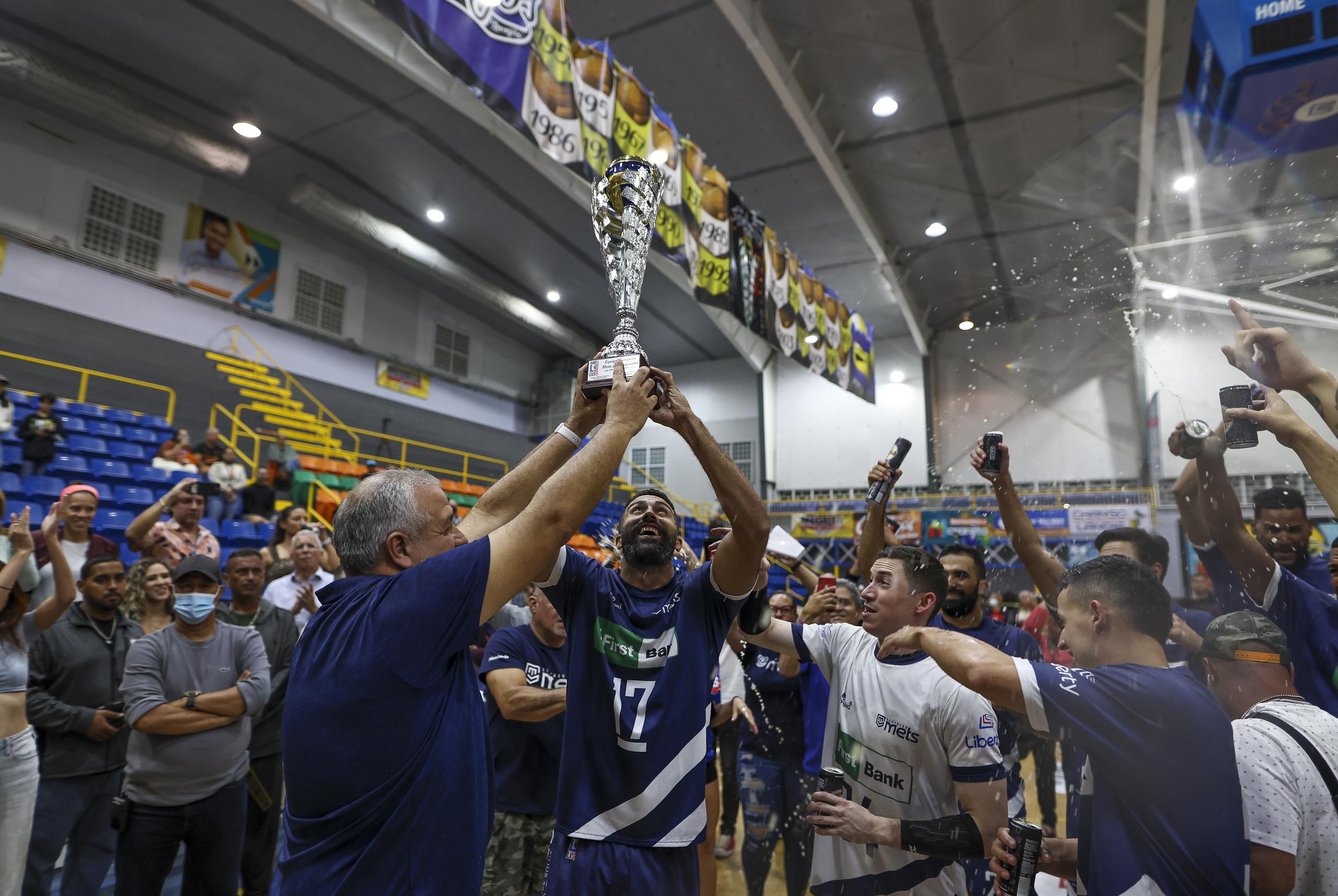 El coapoderado de los Mets, Hugo Pérez, y el opuesto Jean Carlos Ortiz levantan el trofeo de campeones del Voleibol Superior 2022.