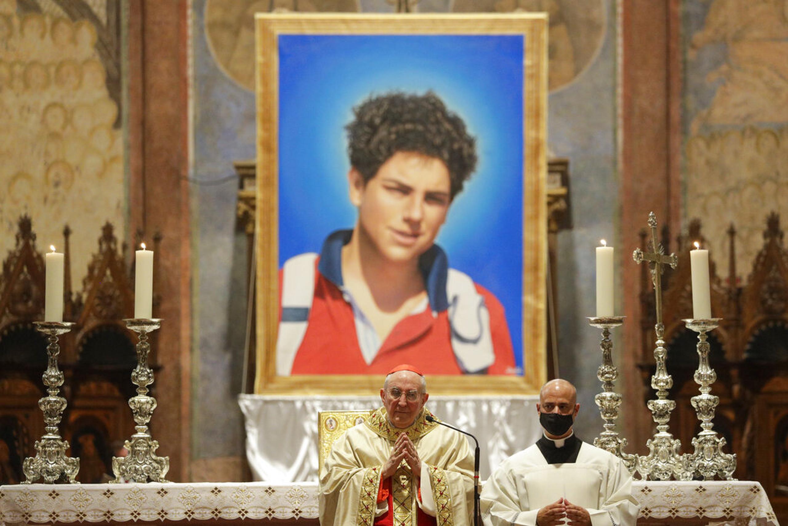 Una imagen del chico italiano Carlo Acutis, de 15 años, que falleció en 2006 de leucemia, es presentada durante su beatificación en una ceremonia a cargo del cardenal Agostino Vallini, al centro, en la Basílica de San Francisco, en Asís, Italia.
