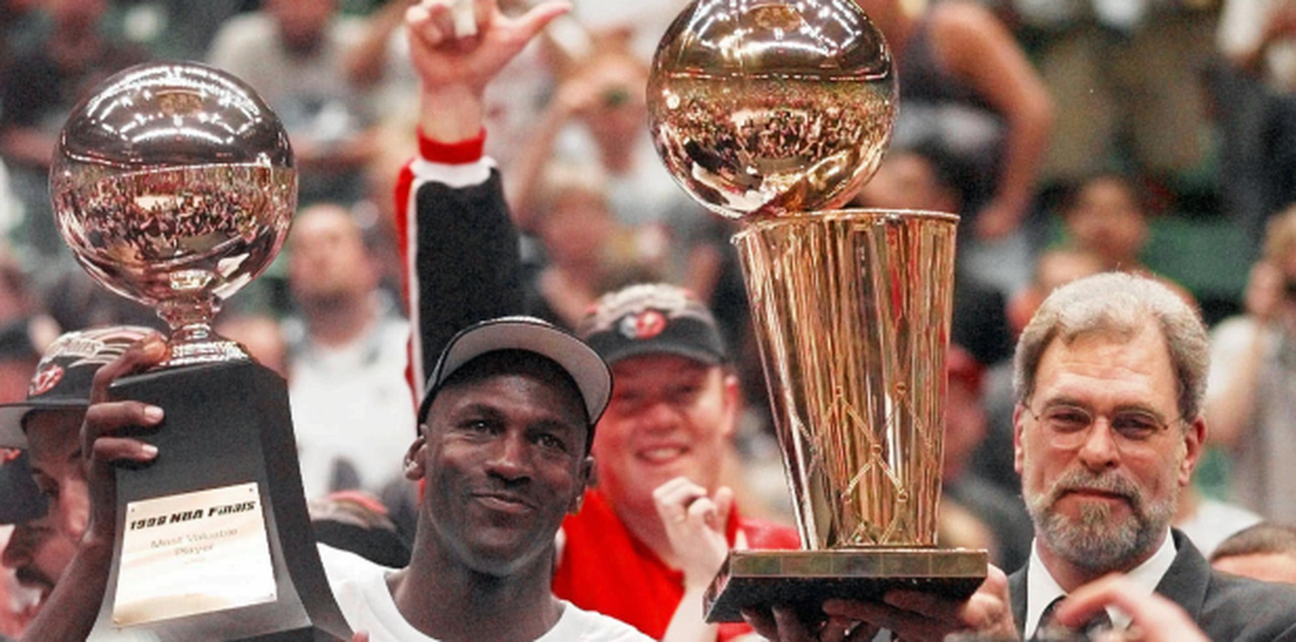 Michael Jordan (derecha), de los Chicago Bulls, mientras cargaba el trofeo de "jugador más valioso" tras ser pieza clave en la victoria de su equipo contra el Jazz en la serie de 1998. A su lado, el entrenador del equipo, Phil Jackson  (Archivo)