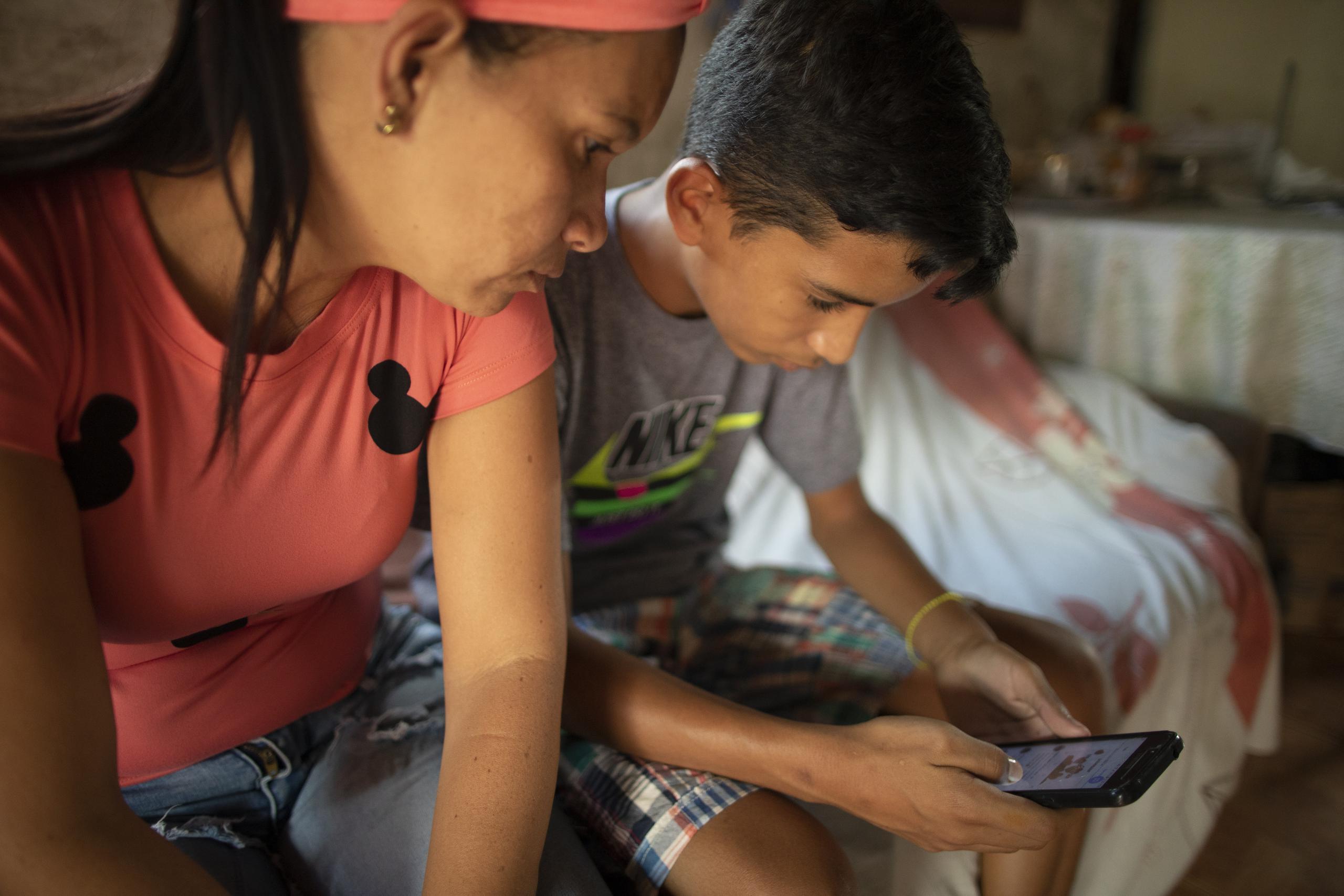 Samuel Andrés Mendoza revisa su cuenta de Twitter, donde vende sus dibujos, con su madre Magdalena Rodríguez en su casa en Barquisimeto, Venezuela, el martes 2 de marzo de 2021.  (AP Foto/Ariana Cubillos)