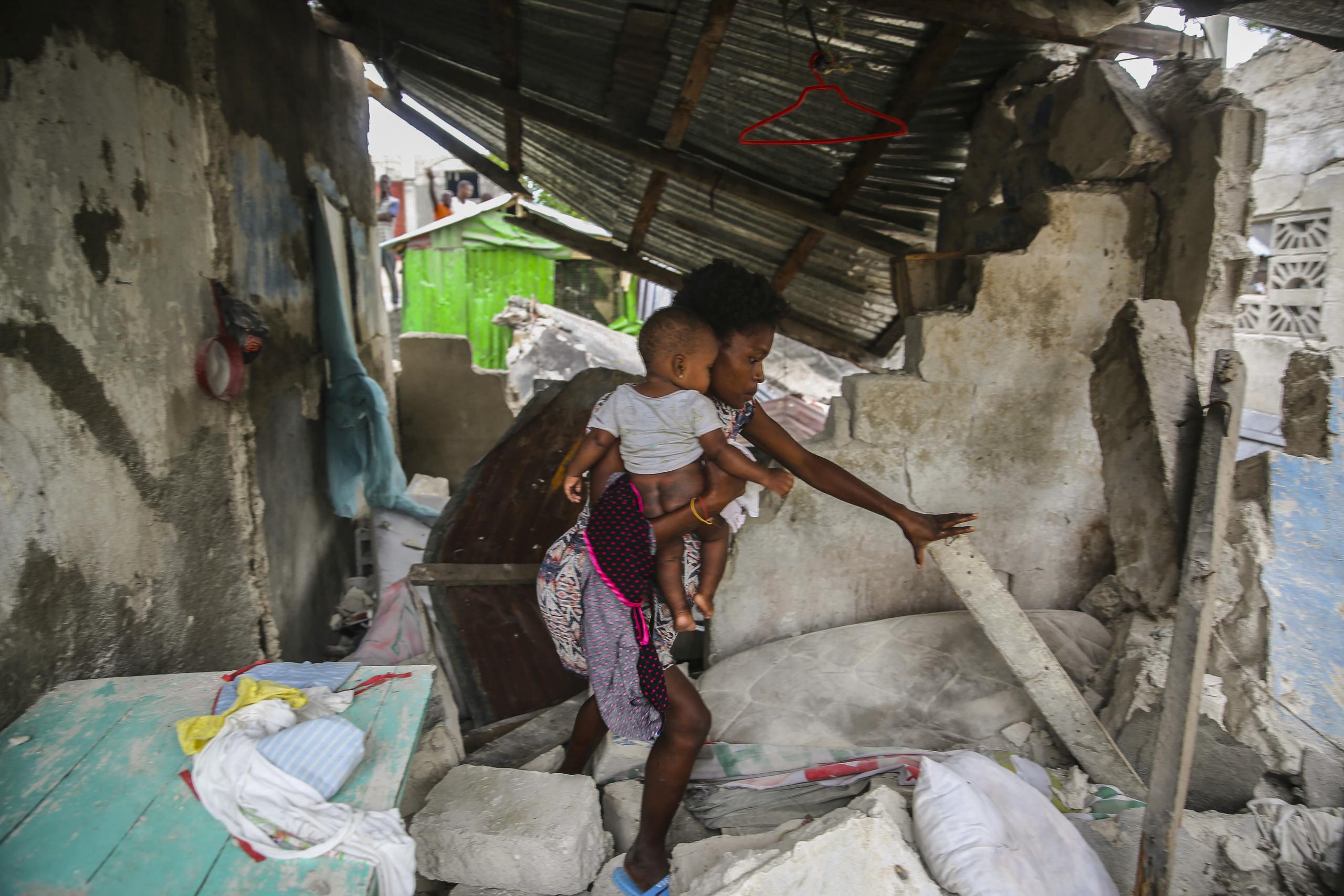 Una mujer carga a su hijo mientras camina entre los restos de su casa destruida por un sismo de 7.2 que sacudió Haití.