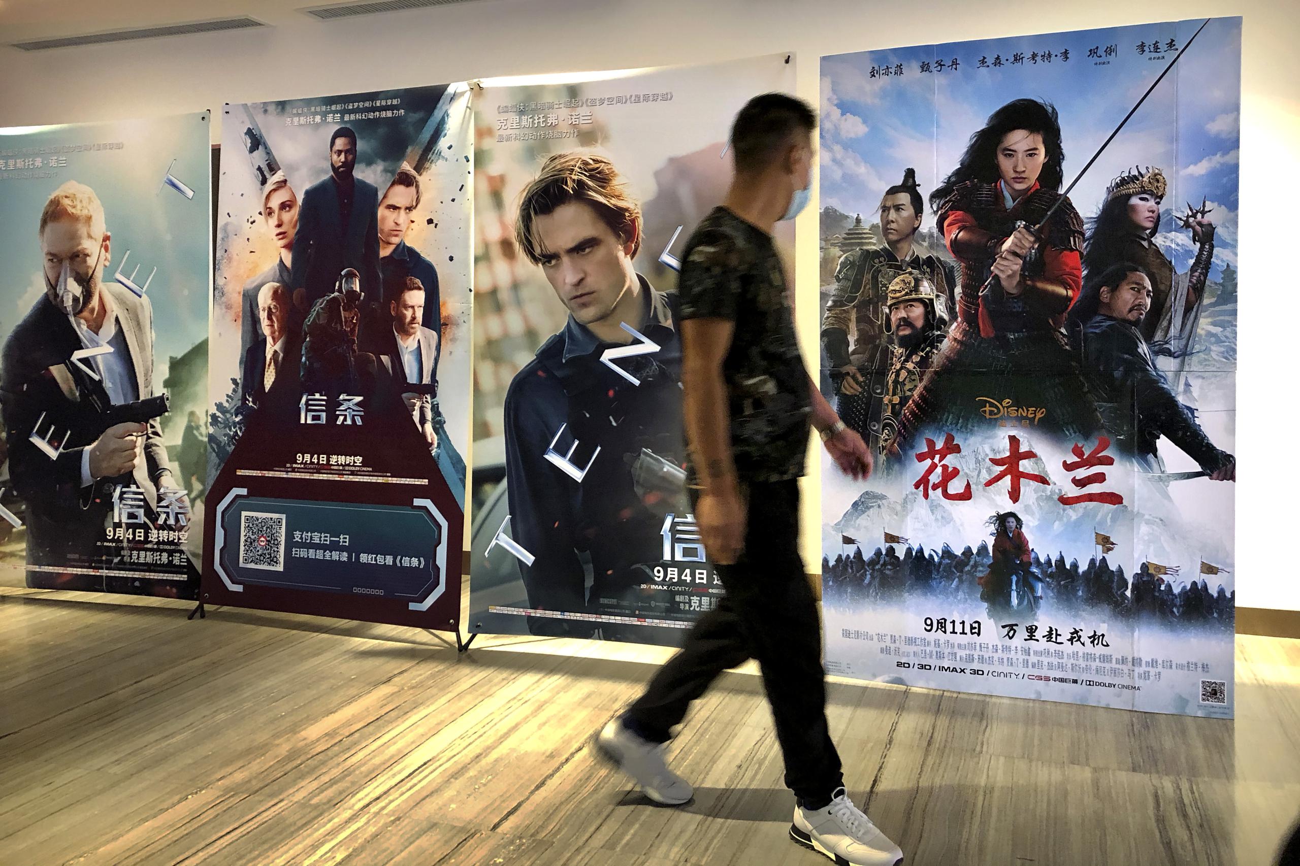 Un hombre con mascarilla pasa junto a un póster de la película de Disney "Mulan" en un cine en Beijing