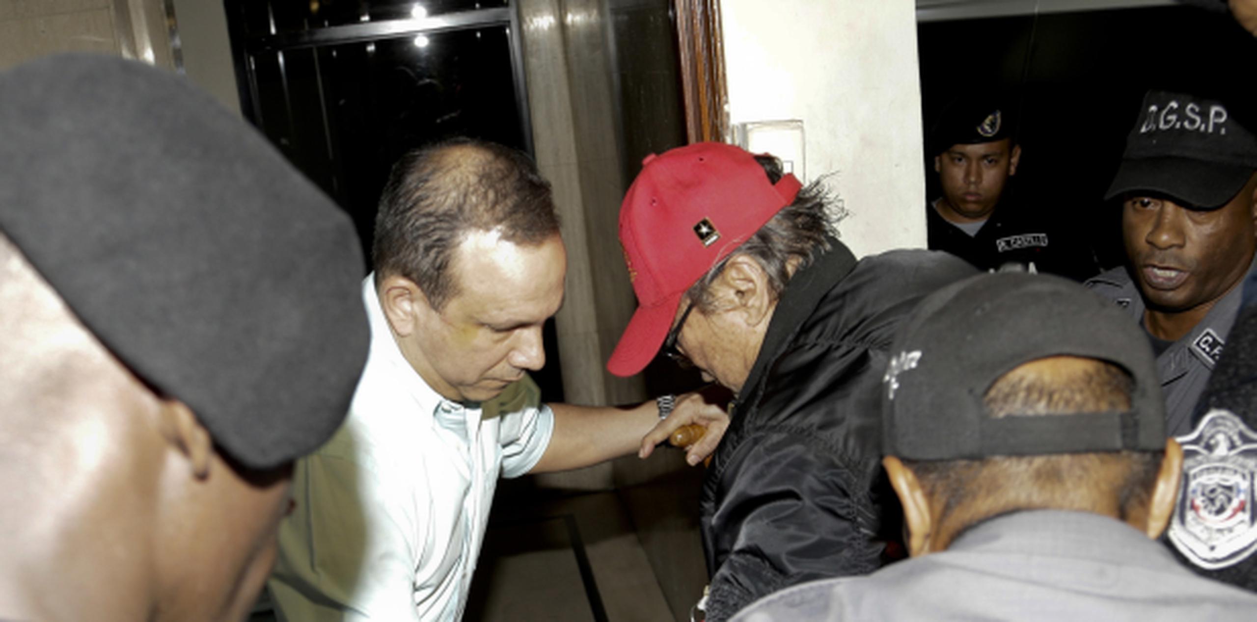 Con gorra roja y rodeado de agentes, el general Noriega comienza a cumplir un periodo de arresto domiciliario. (AP)