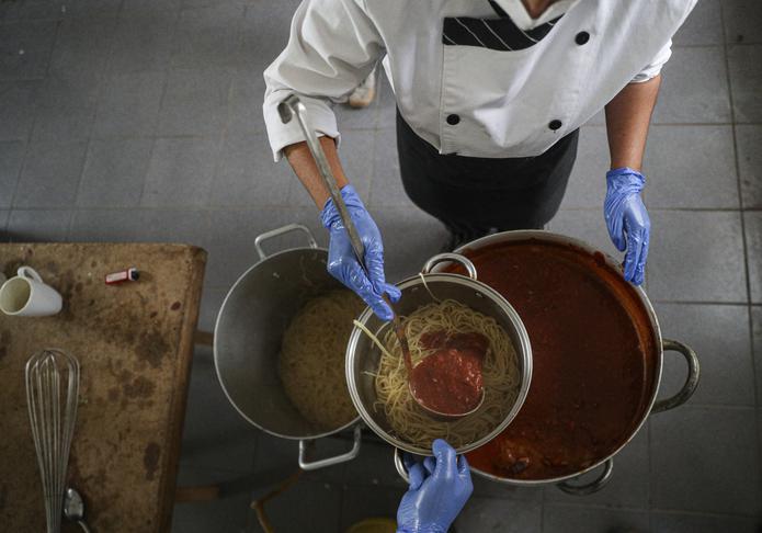 La chef Alejandra Albornoz sirve salsa roja sobre una olla con pasta mientras ella y otros voluntarios se preparan para distribuir comida a vecinos que la pasan mal por falta de ingresos durante la pandemia en El Nocedal a las afueras de Santiago, Chile. (AP)