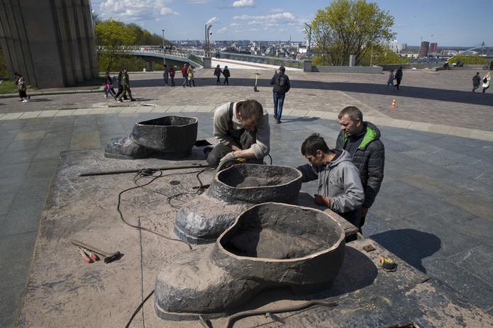 Varios obreros retiran las últimas piezas de una estatua conmemorativa entre Ucrania y Rusia, en Kiev.