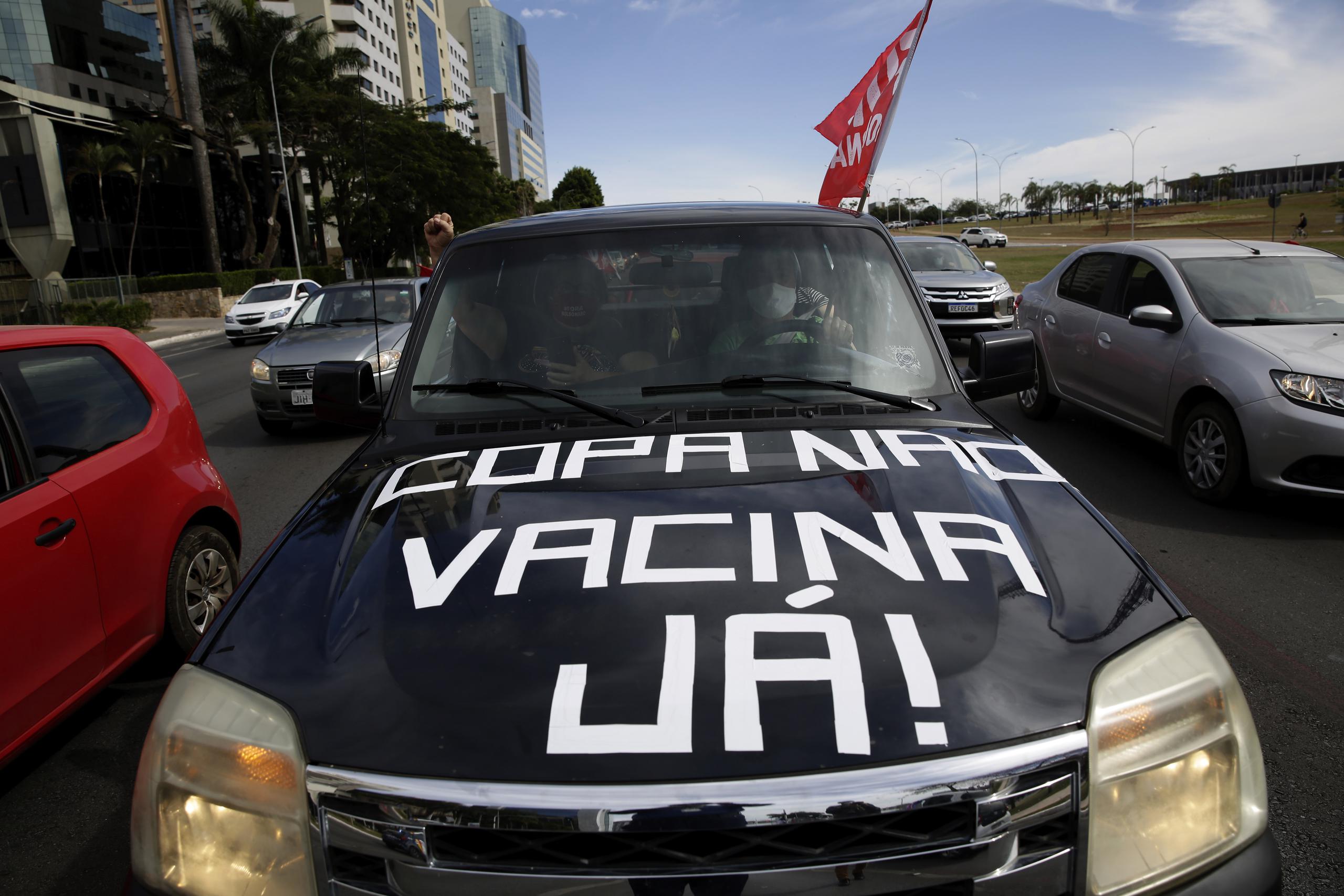 Personas en un auto protestan en Brasilia contra la realización de la Copa América en Brasil debido a la pandemia de coronavirus. El auto tiene escrito en portugués  el mensaje que ha resonado en todo el país: “Copa no, vacunas ya”.