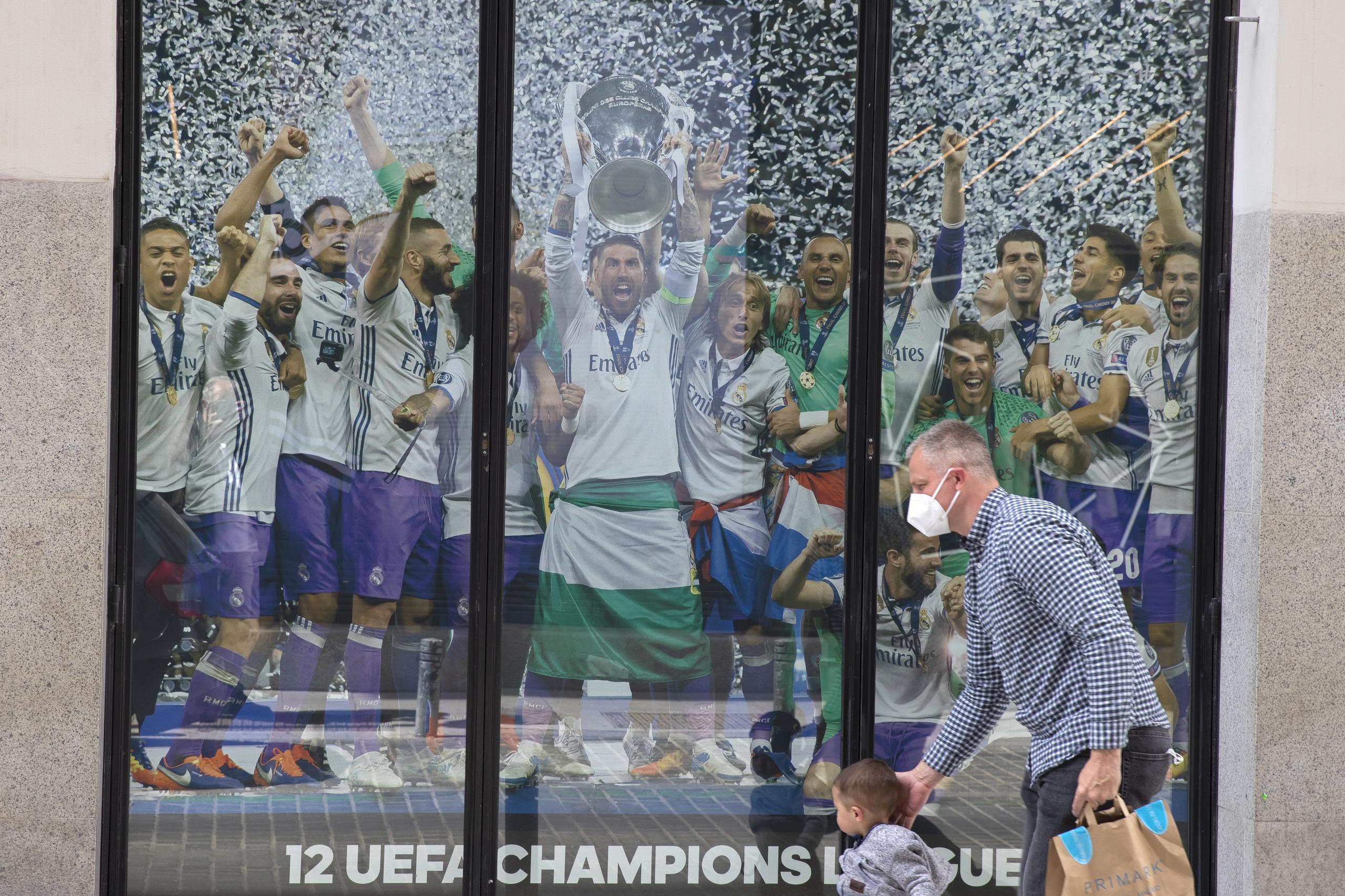 Un hombre y un niño pasan junto a un cartel del Real Madrid. Este equipo es parte del grupo de 12 conjuntos que han anunciado la creación de la Superliga.