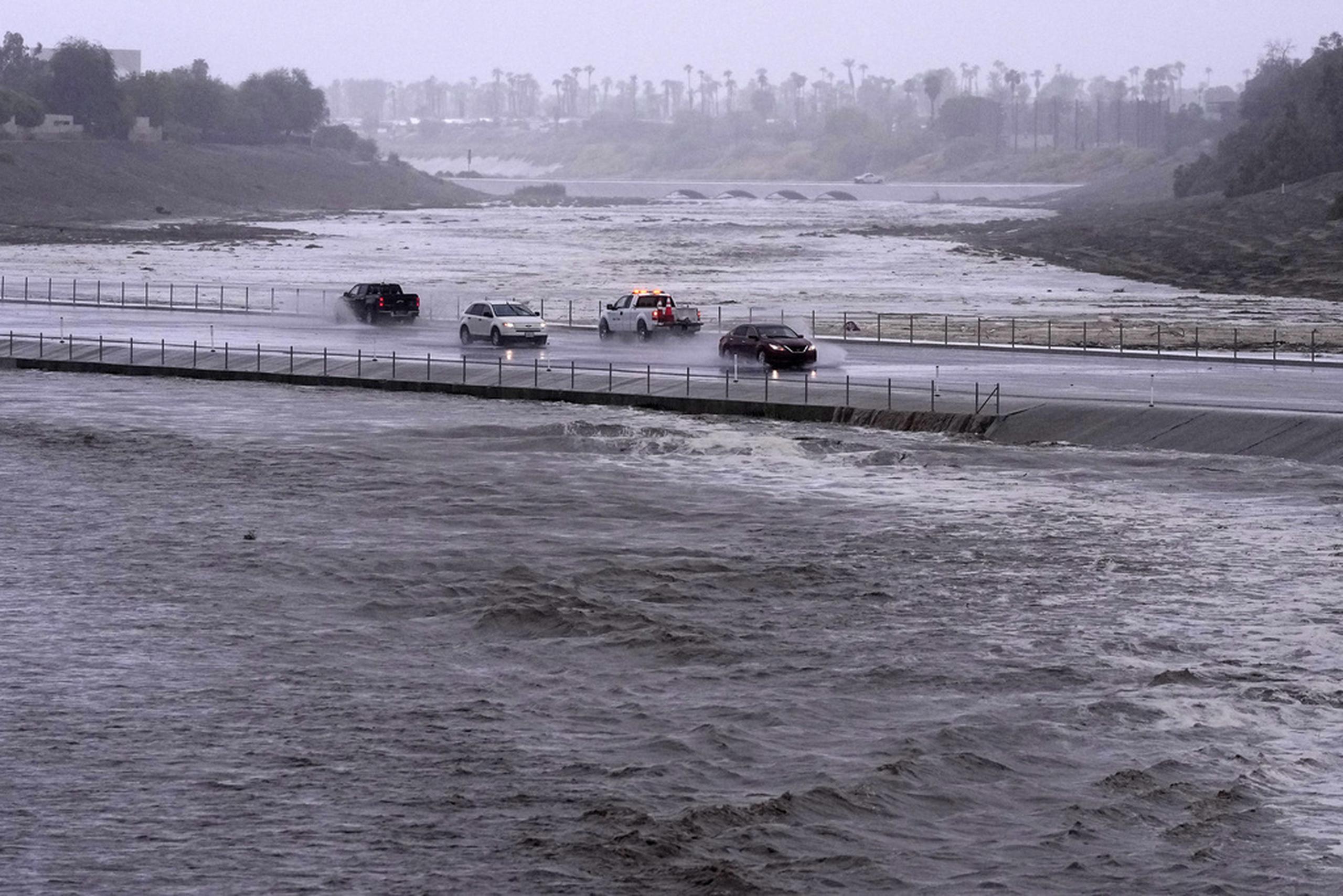 Los vehículos cruzan una cuenca de control de inundaciones que casi llega a la calle, el 20 de agosto de 2023, en Palm Desert, California.