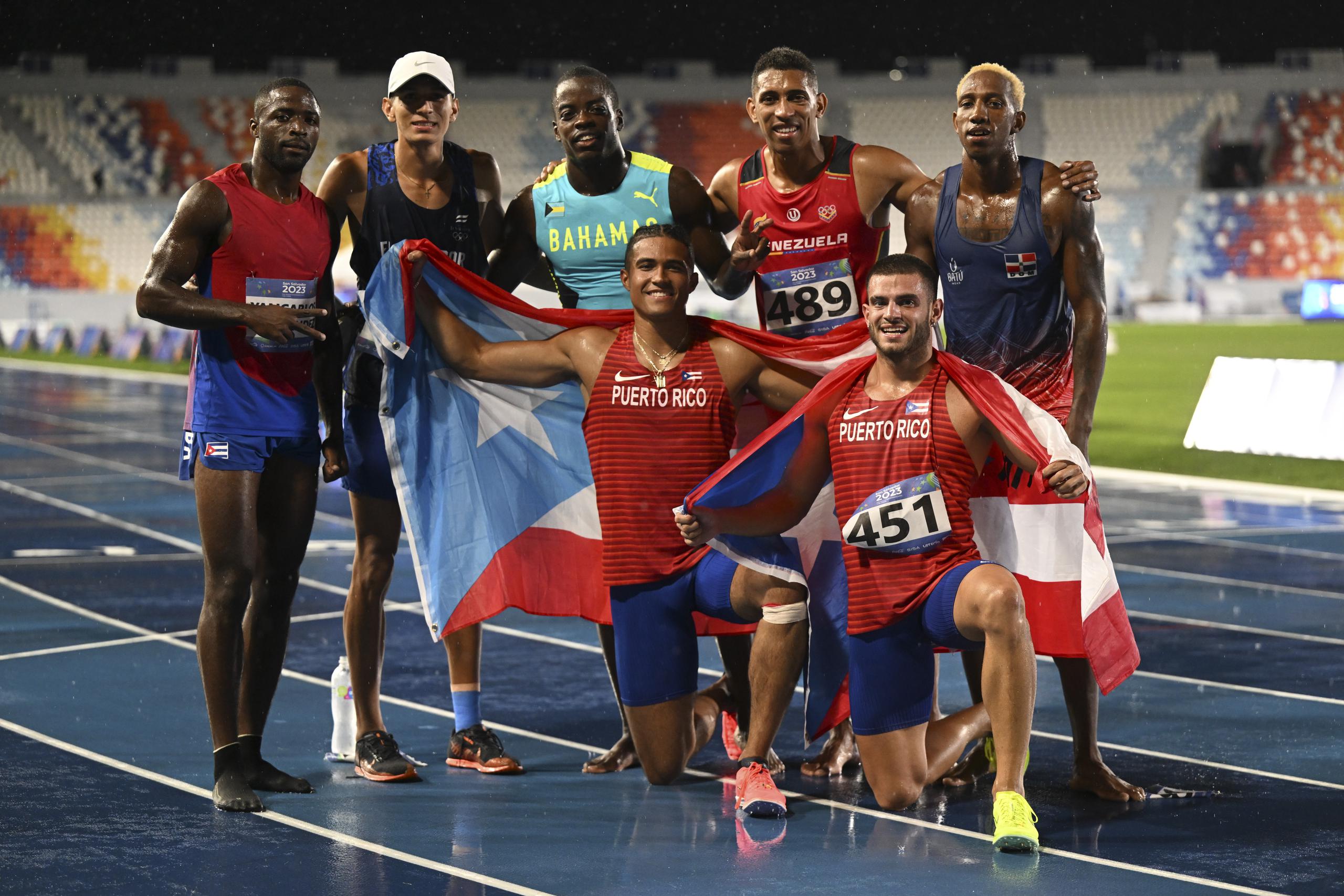 Ayden Owens y Yariel Soto posan, banderas en manos, al concluir el evento de los 1,500 metros junto a otros competidores.