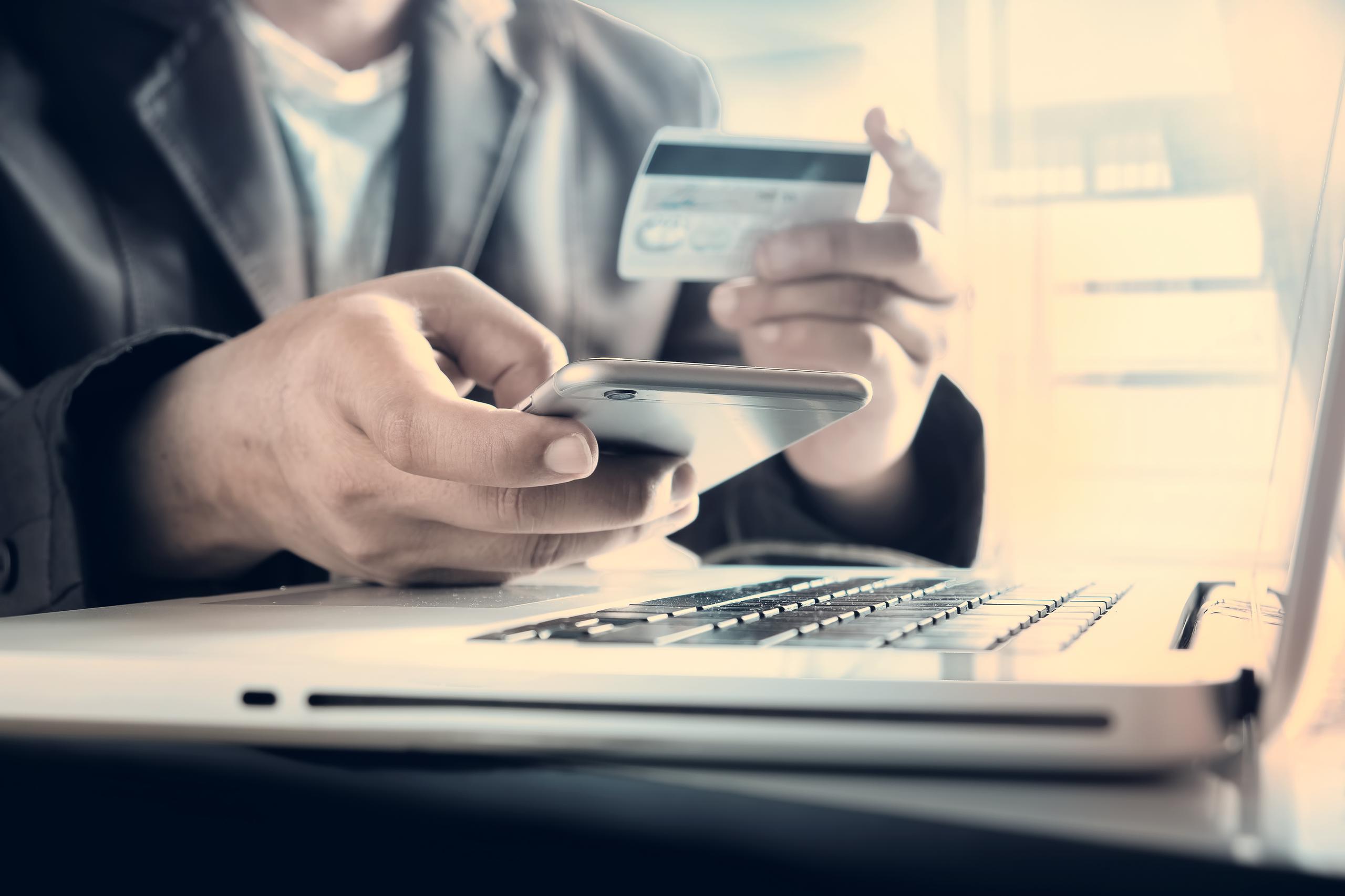 Un hombre sostiene una tarjeta de crédito en la mano mientras realiza una transacción electrónica.
