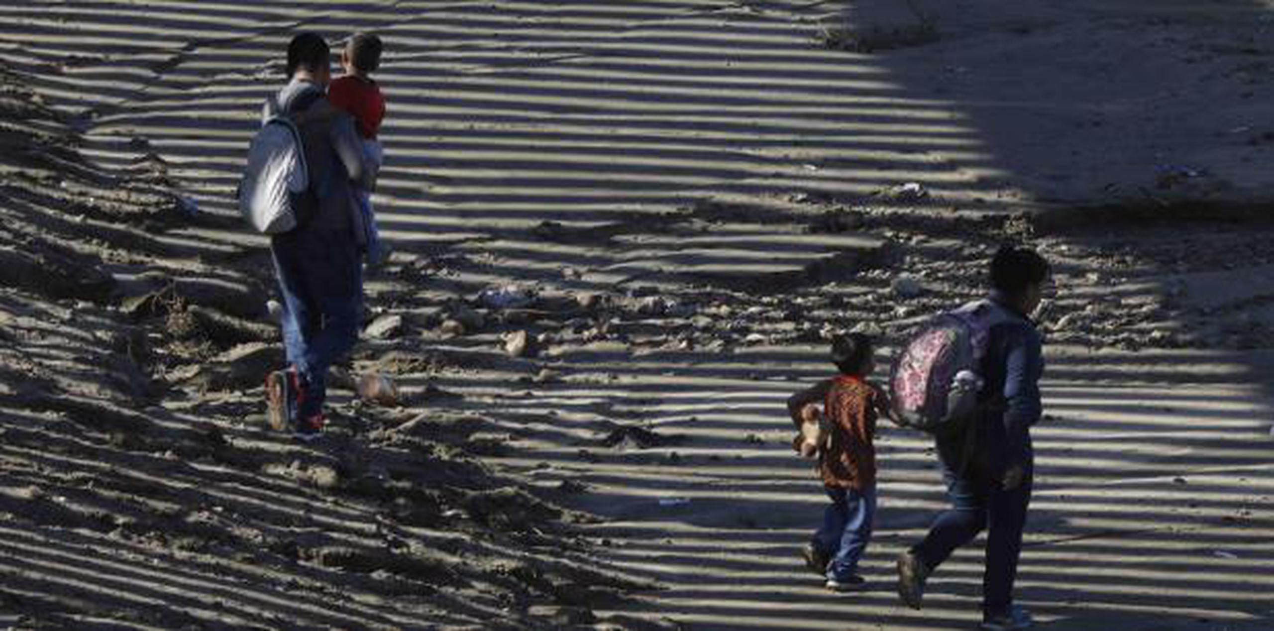 Una familia de indocumentados camina cerca del muro existente en la frontera con Estados Unidos. (AP)