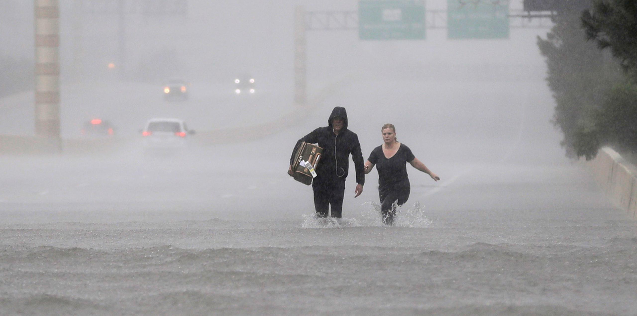 Dos personas caminan por una zona de la Interestatal 610 inundada por la tormenta tropical Harvey. (AP)