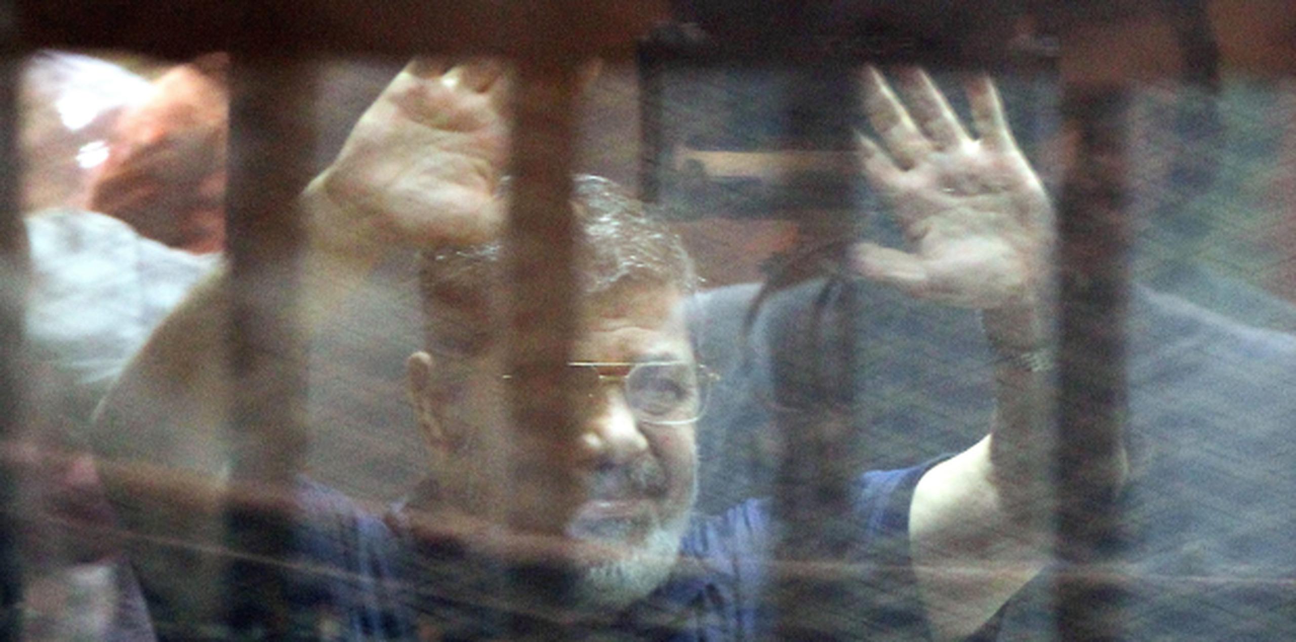 Desde una celda, Mohammed Morsi saluda a simpatizantes el día de su sentencia de muerte. (AP)