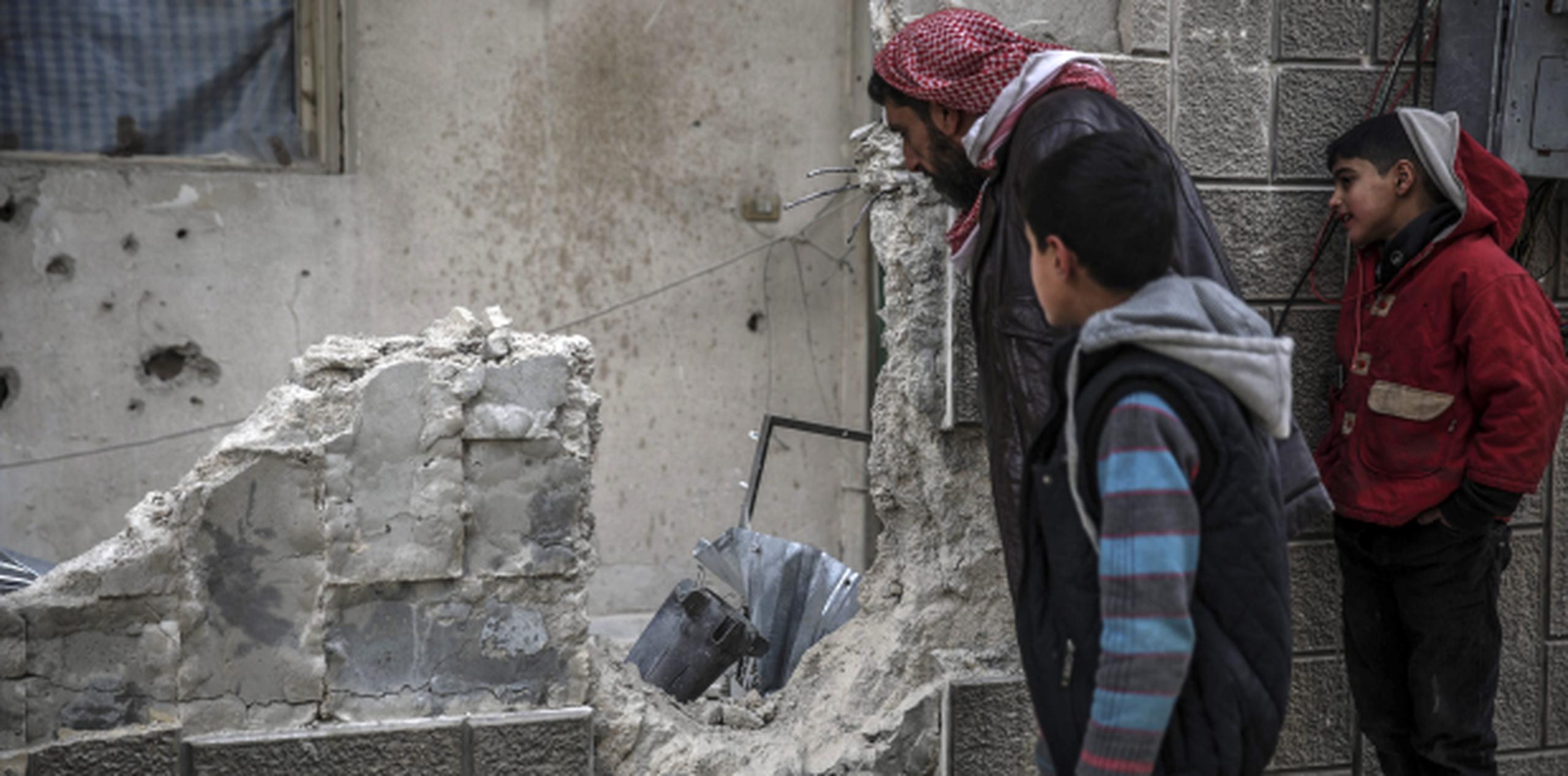 Curiosos inspeccionan los restos de una bomba tras un ataque aéreo en Douma, a las afueras de Damasco. (EFE)