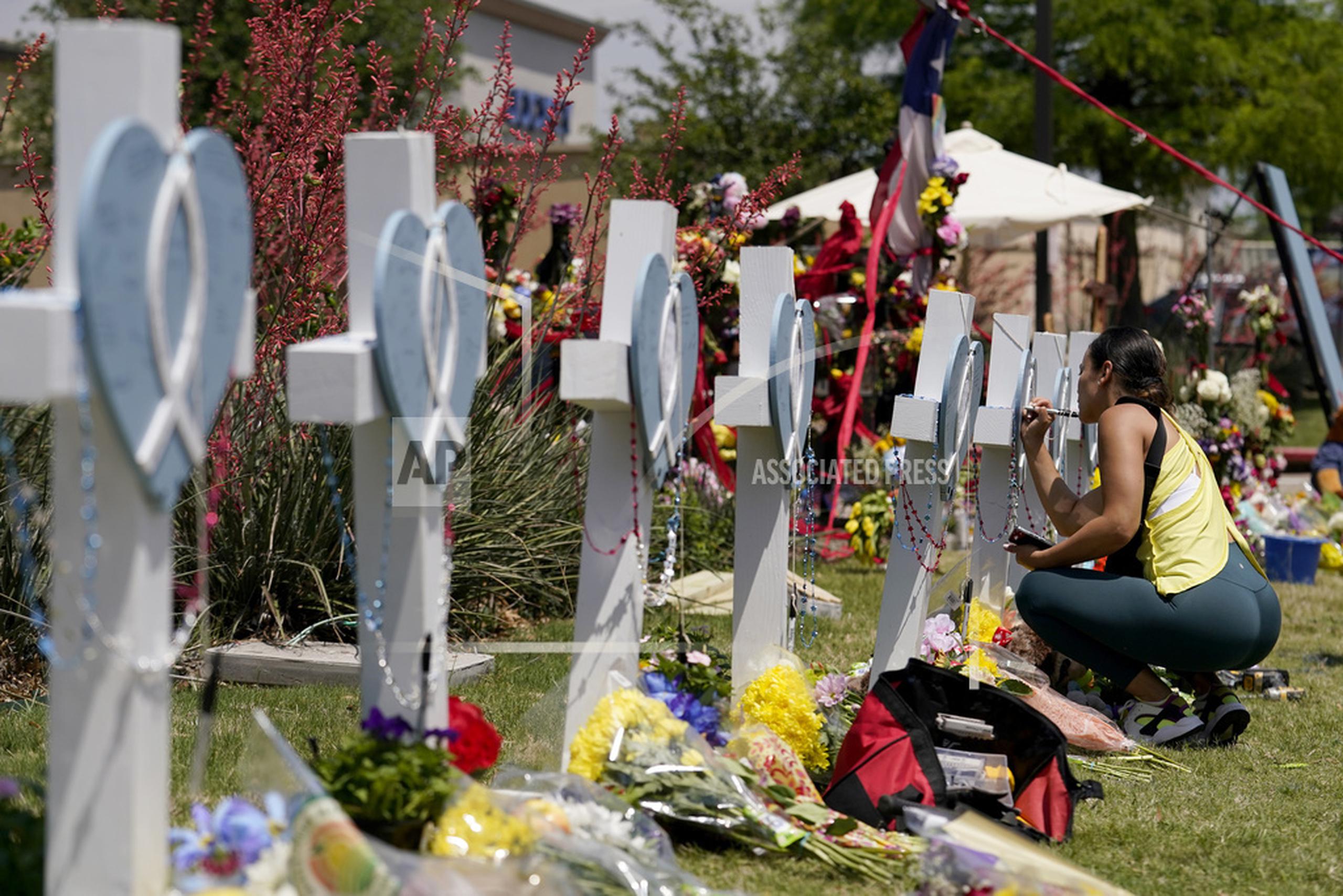 Una mujer firma una cruz alineada junto a otras en un altar improvisado en honor de las víctimas de una masacre, el lunes 8 de mayo de 2023, en Allen, Texas. (AP Foto/Tony Gutierrez)