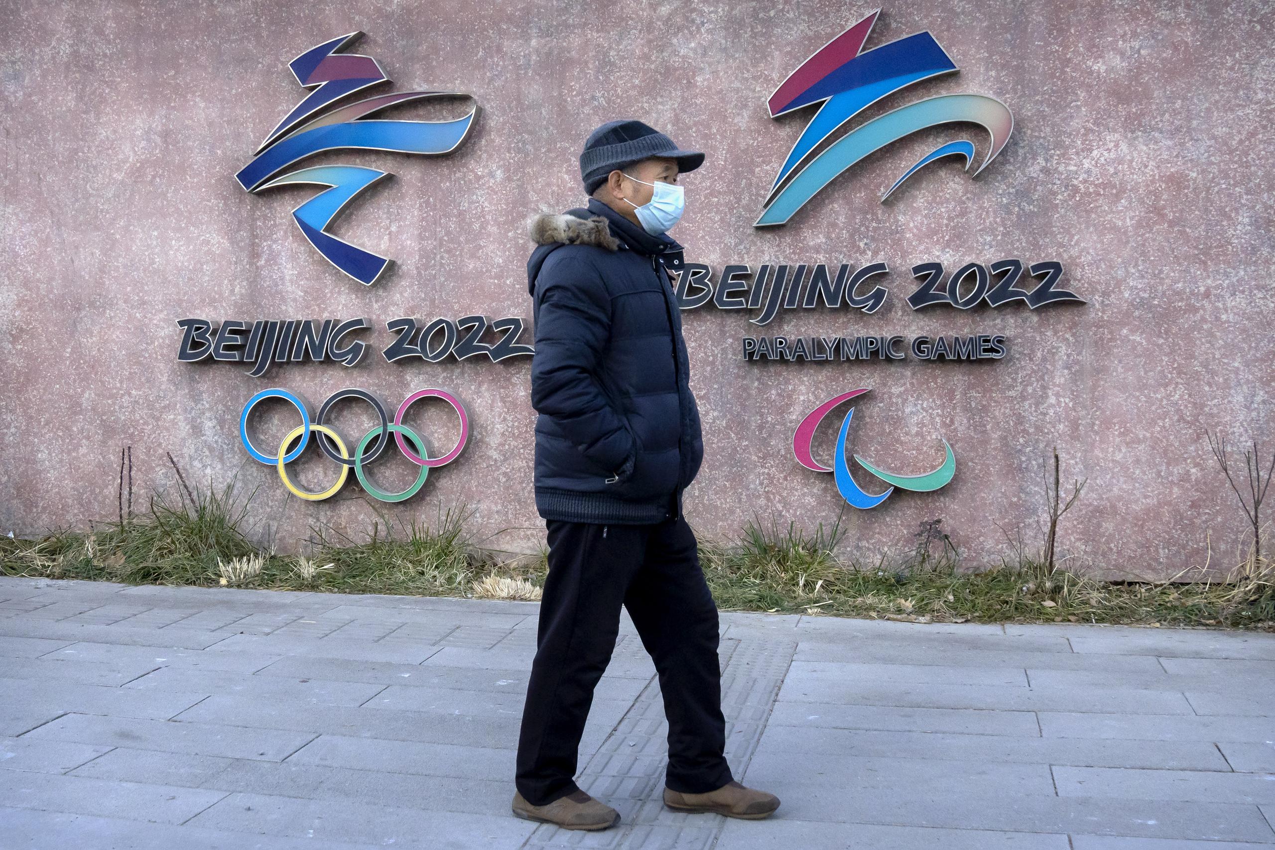 Un hombre, con mascarilla para protegerse del coronavirus, pasa por delante de los logos de los Juegos Olímpicos y Paralímpicos de Invierno de Beijing 2022, en el exterior de la sede del comité organizador, en Beijing, el 16 de diciembre de 2021.