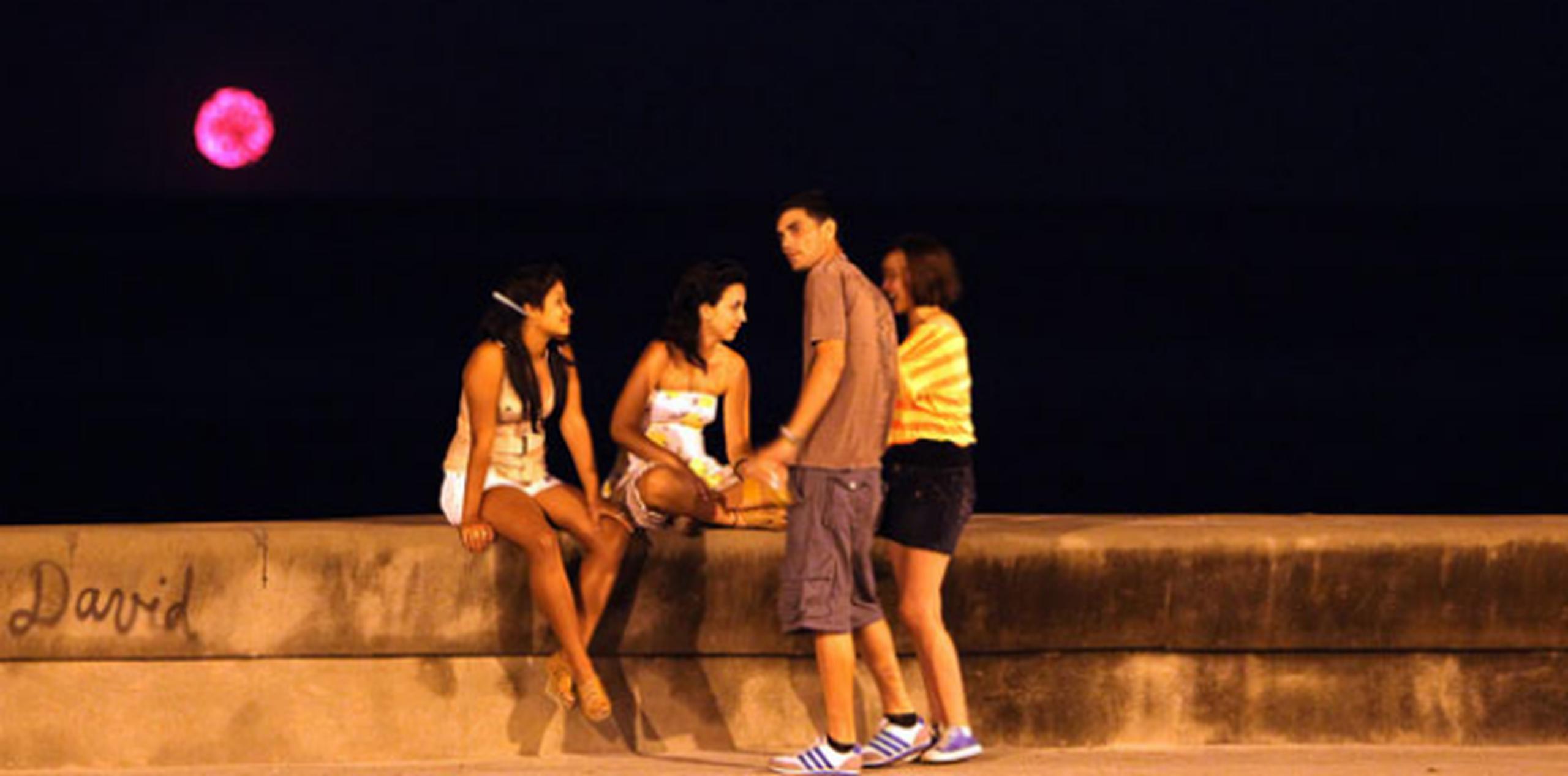 Jóvenes conversan mientras en el fondo se observan los fuegos artificiales lanzados por la flotilla del exilio cubano, en el malecón de La Habana. (EFE)
