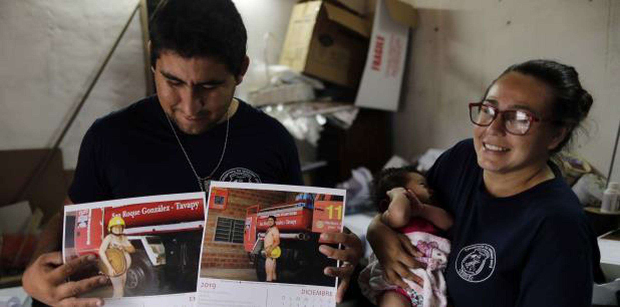 La bombera Fátima Olmedo sostiene a su hija de dos meses Samara mientras su esposo, Rodrigo Giménez, muestra las páginas del calendario donde salen desnudos, en Asunción, Paraguay. (AP / Jorge Saenz)