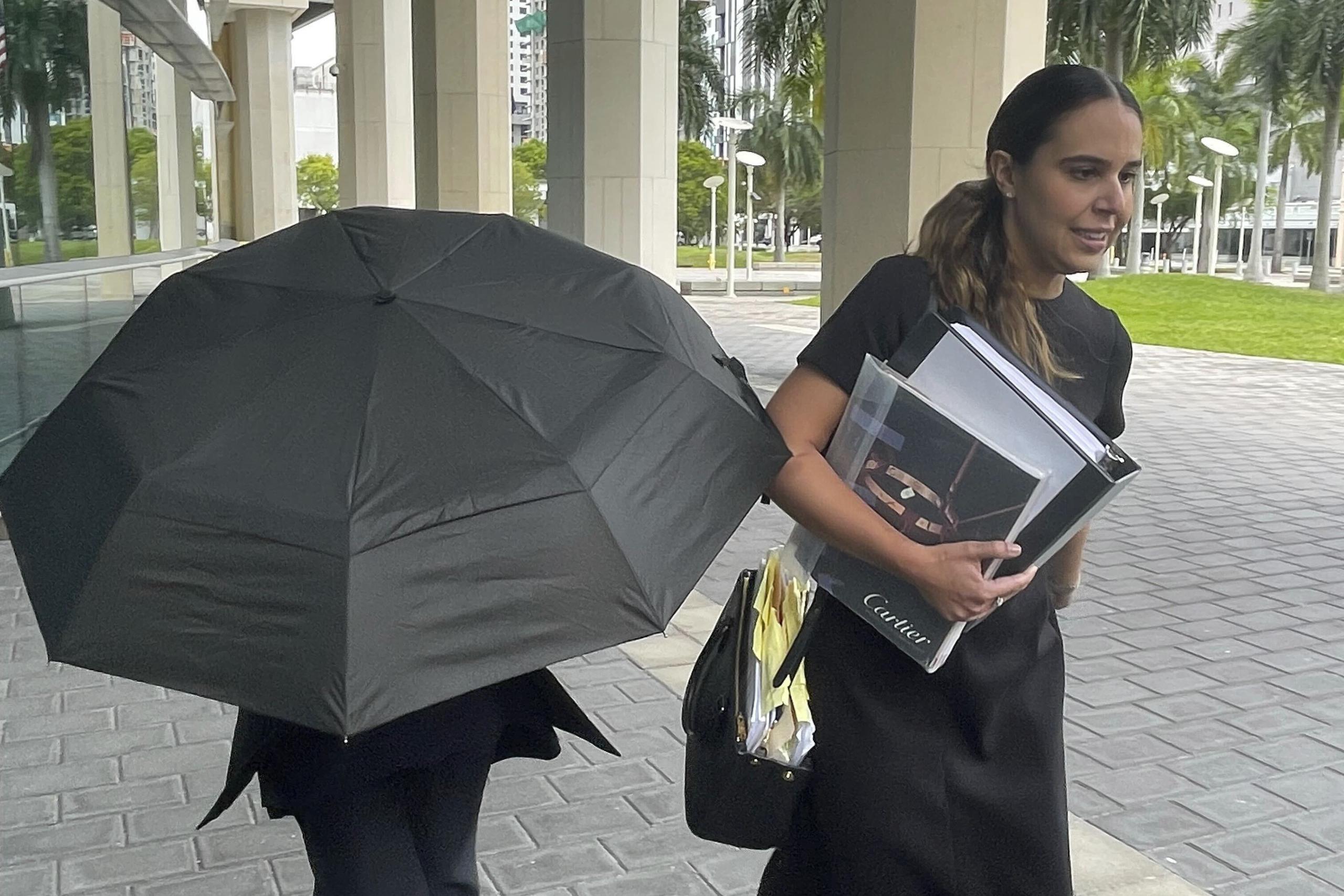 La famosa diseñadora de bolsos Nancy González se esconde bajo un paraguas mientras camina con su abogada Andrea López afuera del tribunal federal en Miami (AP Foto/Josh Goodman).