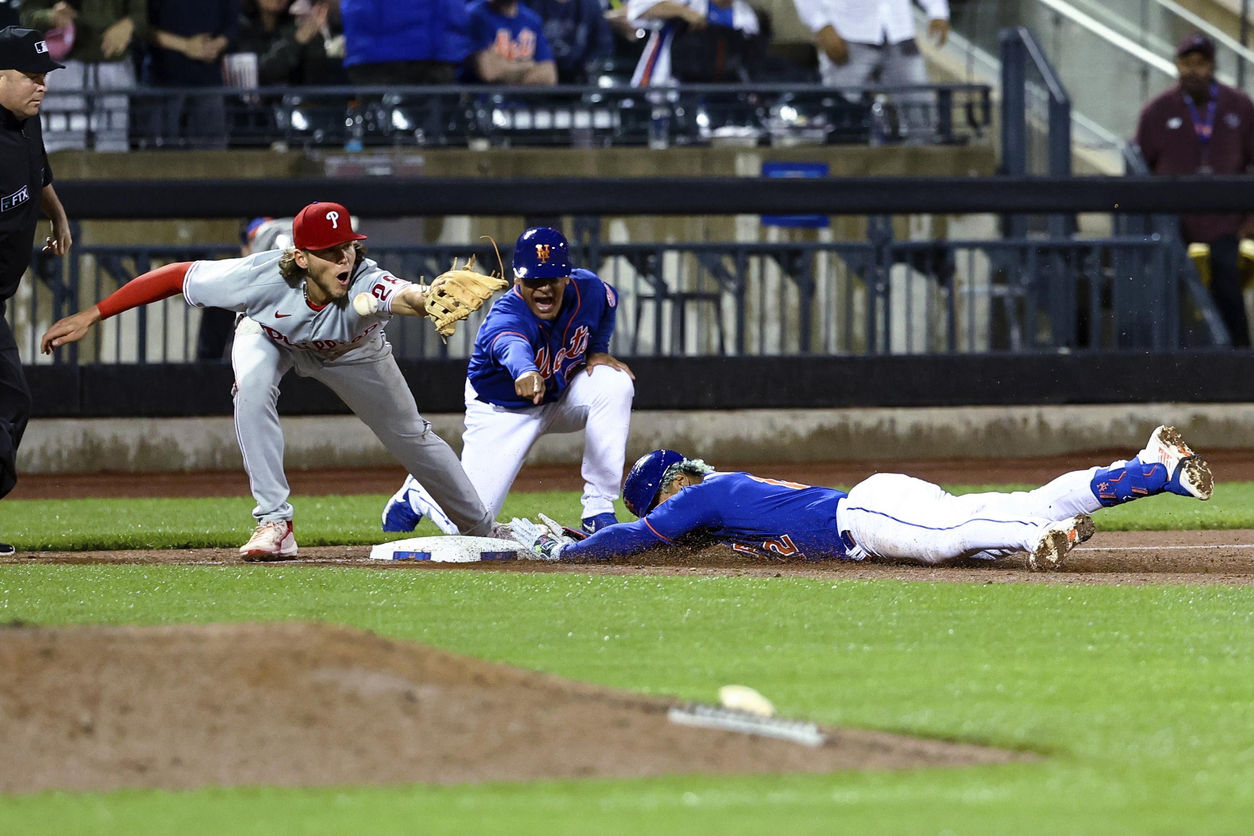 El boricua Francisco Lindor, de los Mets de Nueva York, se desliza a salvo en tercera base mientras el el antesalista de los Phillies, Alec Bohm, espera el tiro y el coach boricua de los Mets, Joey Cora, gesticula.