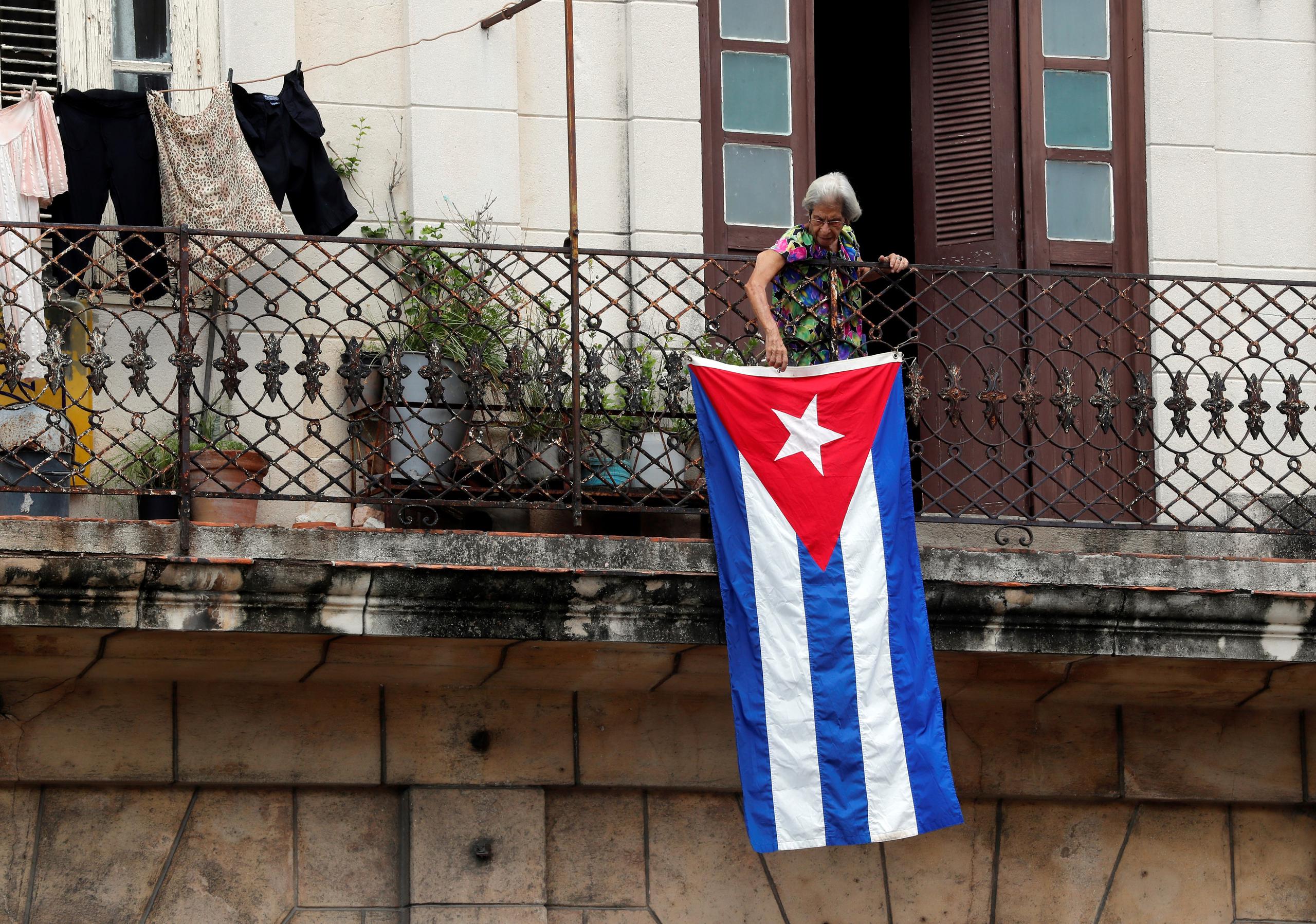 Una mujer sale al balcón donde se expone una bandera cubana, en La Habana, Cuba. EFE/Ernesto Mastrascusa
