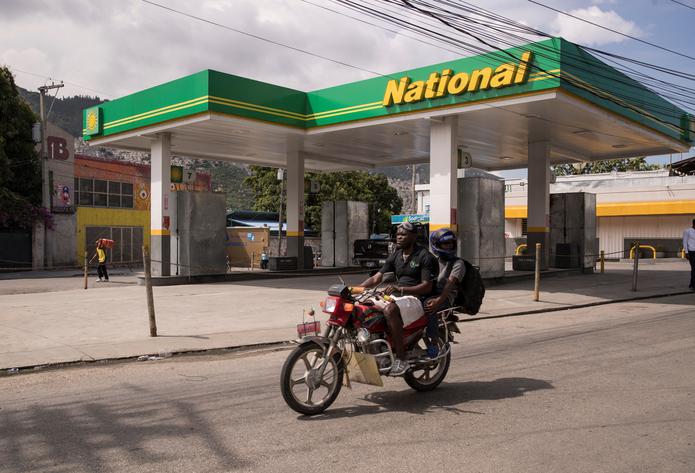 Hombres en motocicleta cruzan frente a una estación de suministro de gasolina que no está prestando servicio al público hoy, en Puerto Príncipe.