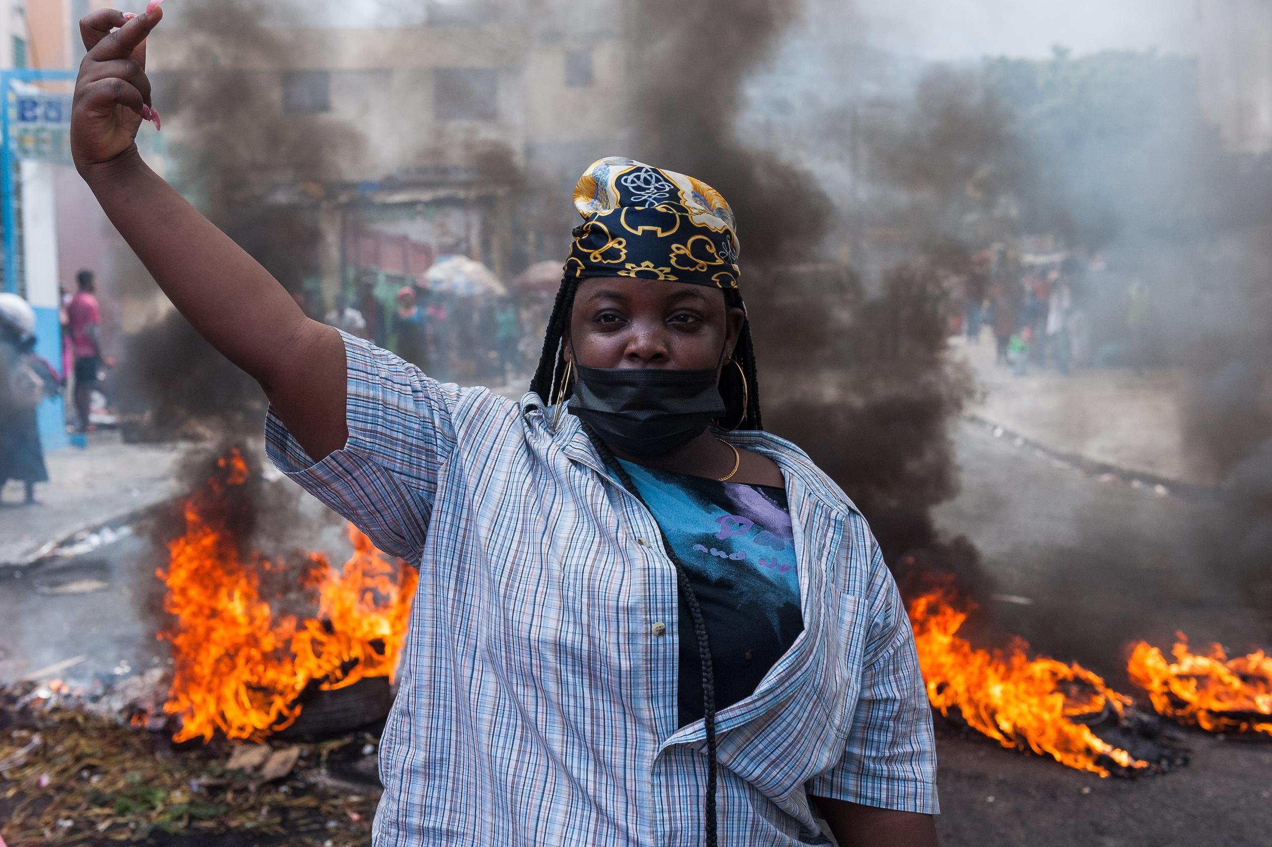 Una mujer muestra una señal con su mano junto a una barricada en llamas durante una jornada de protesta, el 6 de enero de 2022, en Pétion-ville (Haití). EFE/ Johnson Sabin
