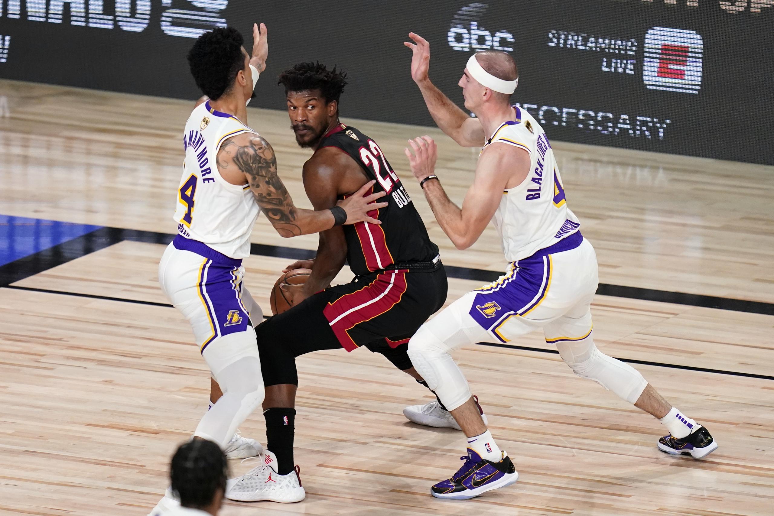 Jimmy Butler (al centro) del Heat de Miami, busca pasar contra Danny Green (14) y Alex Caruso (4), de los Lakers de Los Angeles, durante la primera mitad del Juego 6 de las Finales de la NBA.