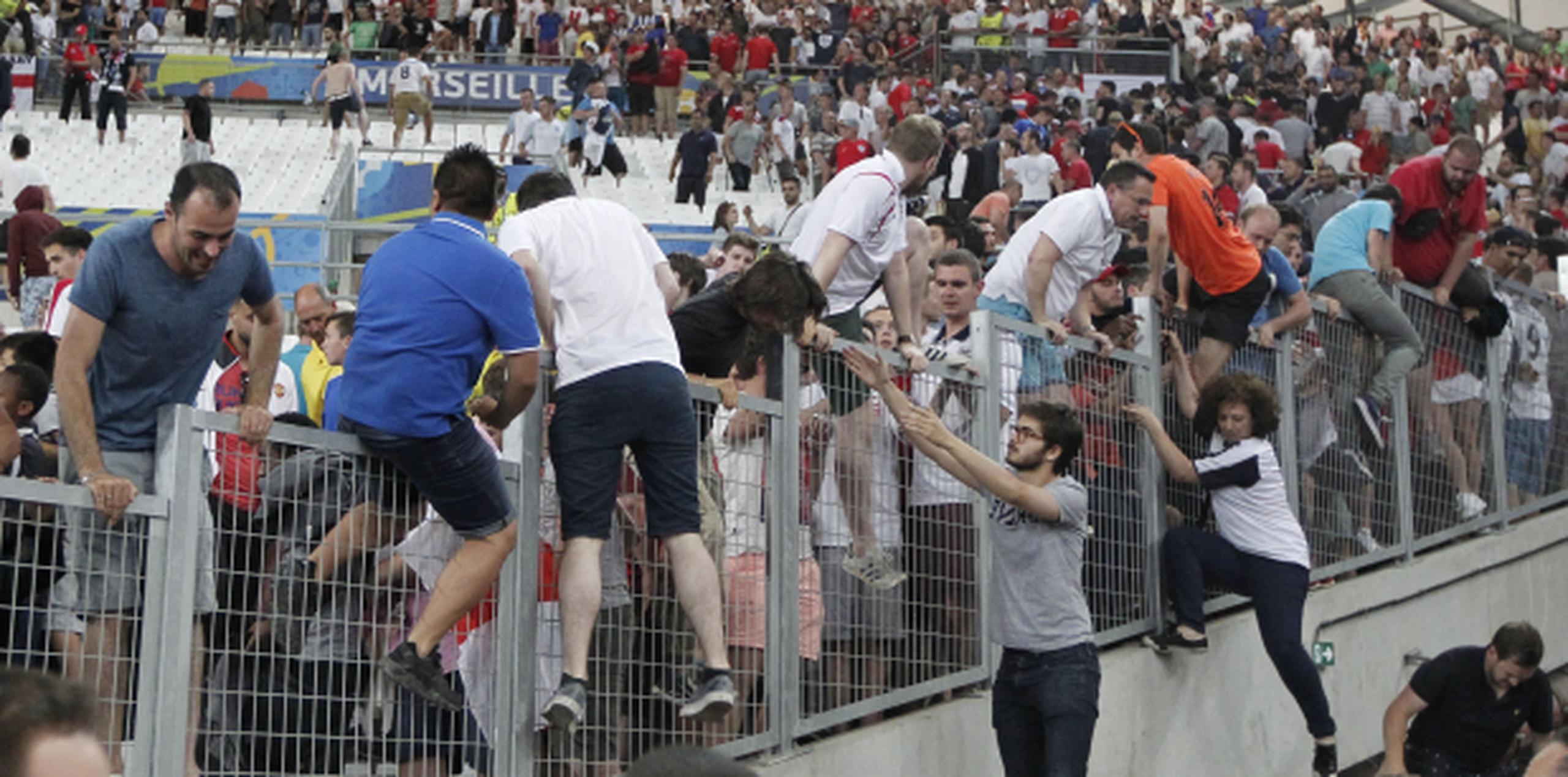 Espectadores brincan por encima de vallas protectoras para escapar de la violencia desatada en los graderíos por grupos de fanáticos al terminar el partido entre Inglaterra y Rusia. (AP/Thanassis Stavrakis)