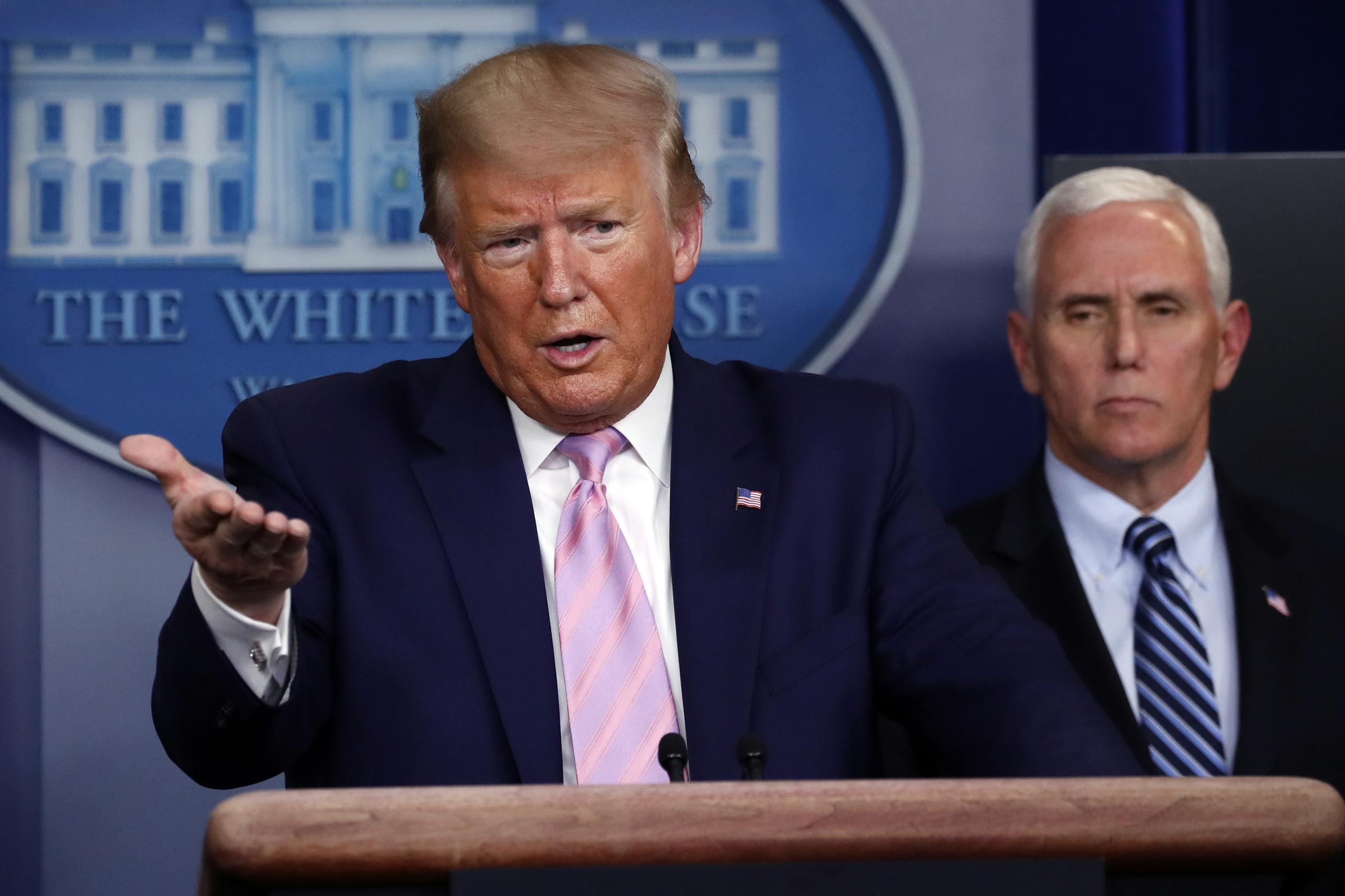 El presidente Donald Trump habla con los reporteros en la sala de prensa de la Casa Blanca, mientras el vicepresidente Mike Pence lo escucha