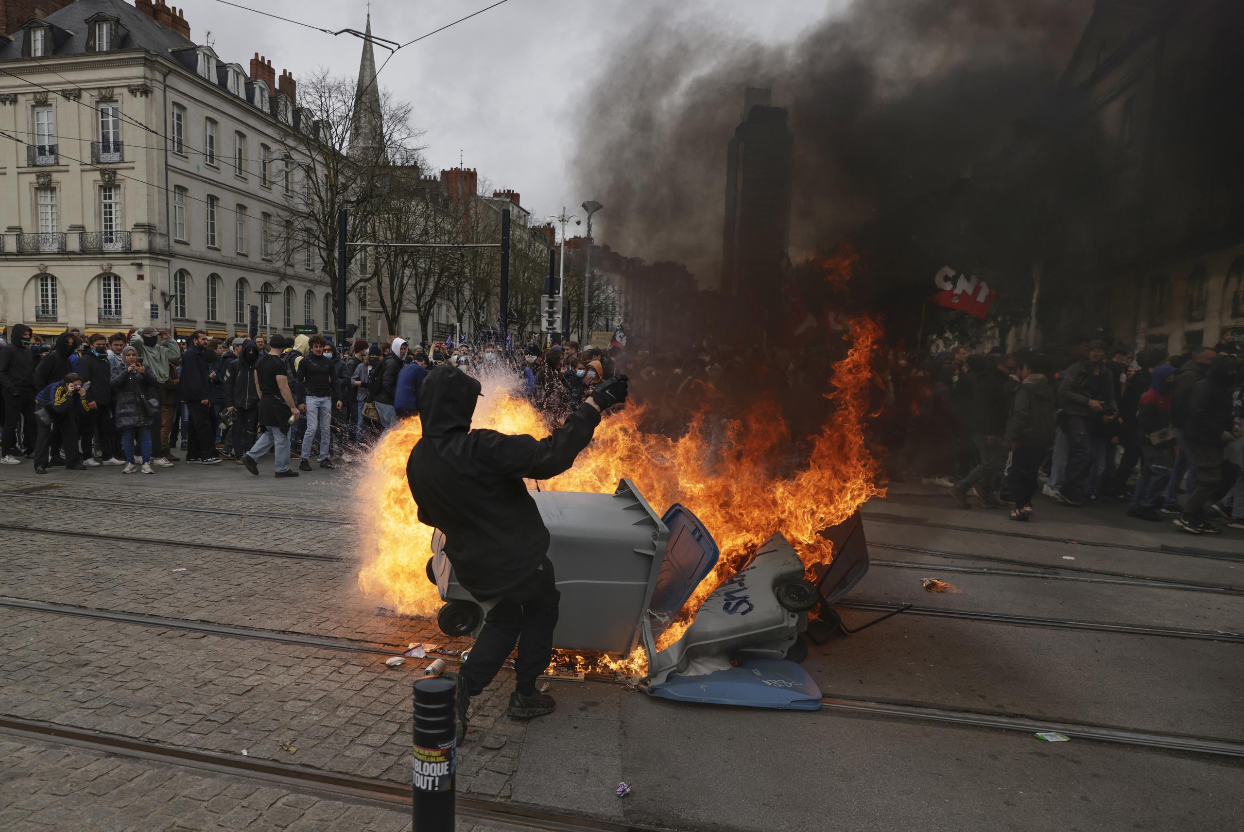 Un manifestante está parado junto a un contenedor de basura en llamas durante una manifestación en Nantes, occidente de Francia. (AP).