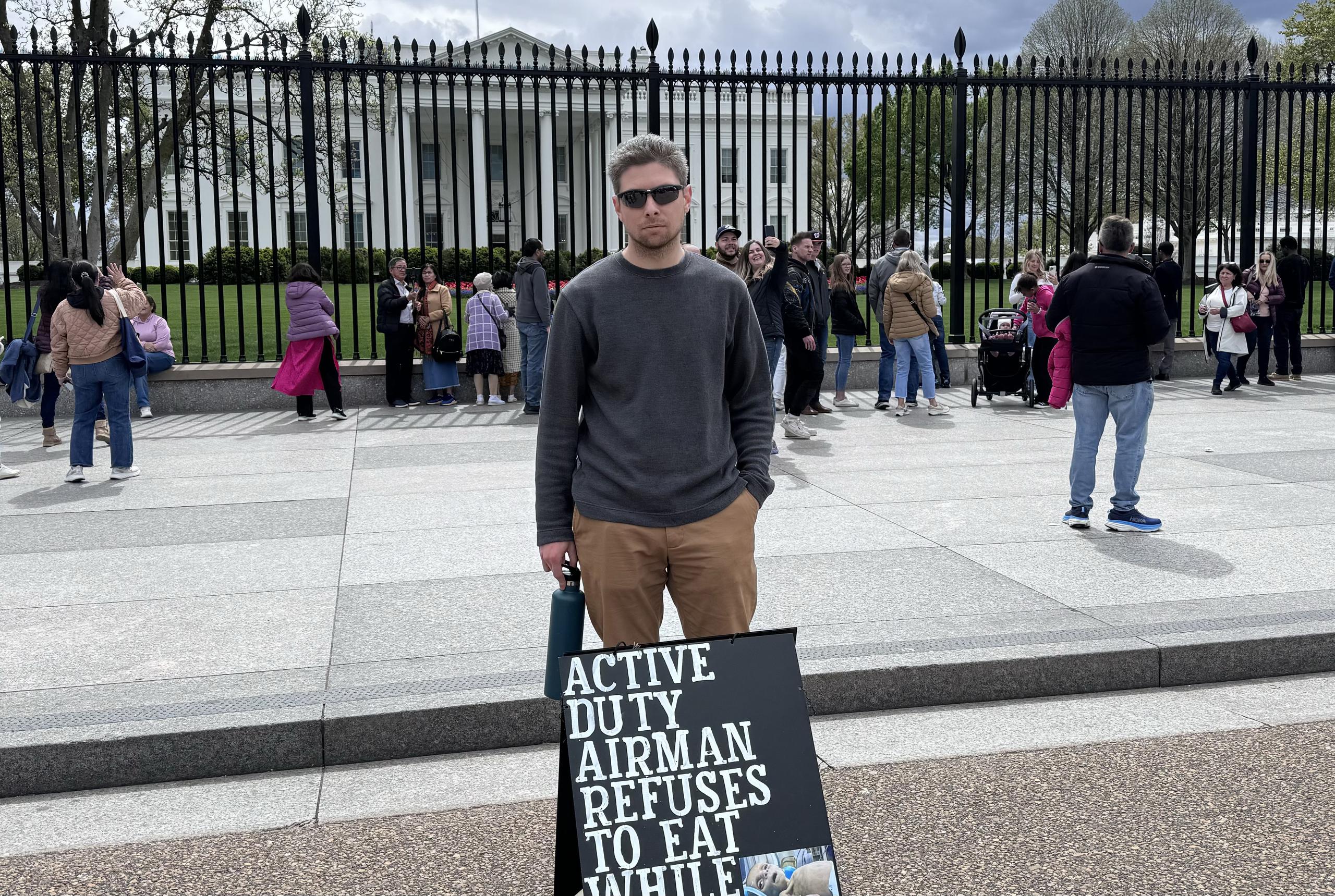 Larry Hebert  posa junto a la pancarta que dice "Aviador en servicio activo se niega a comer mientras Gaza muere de hambre".