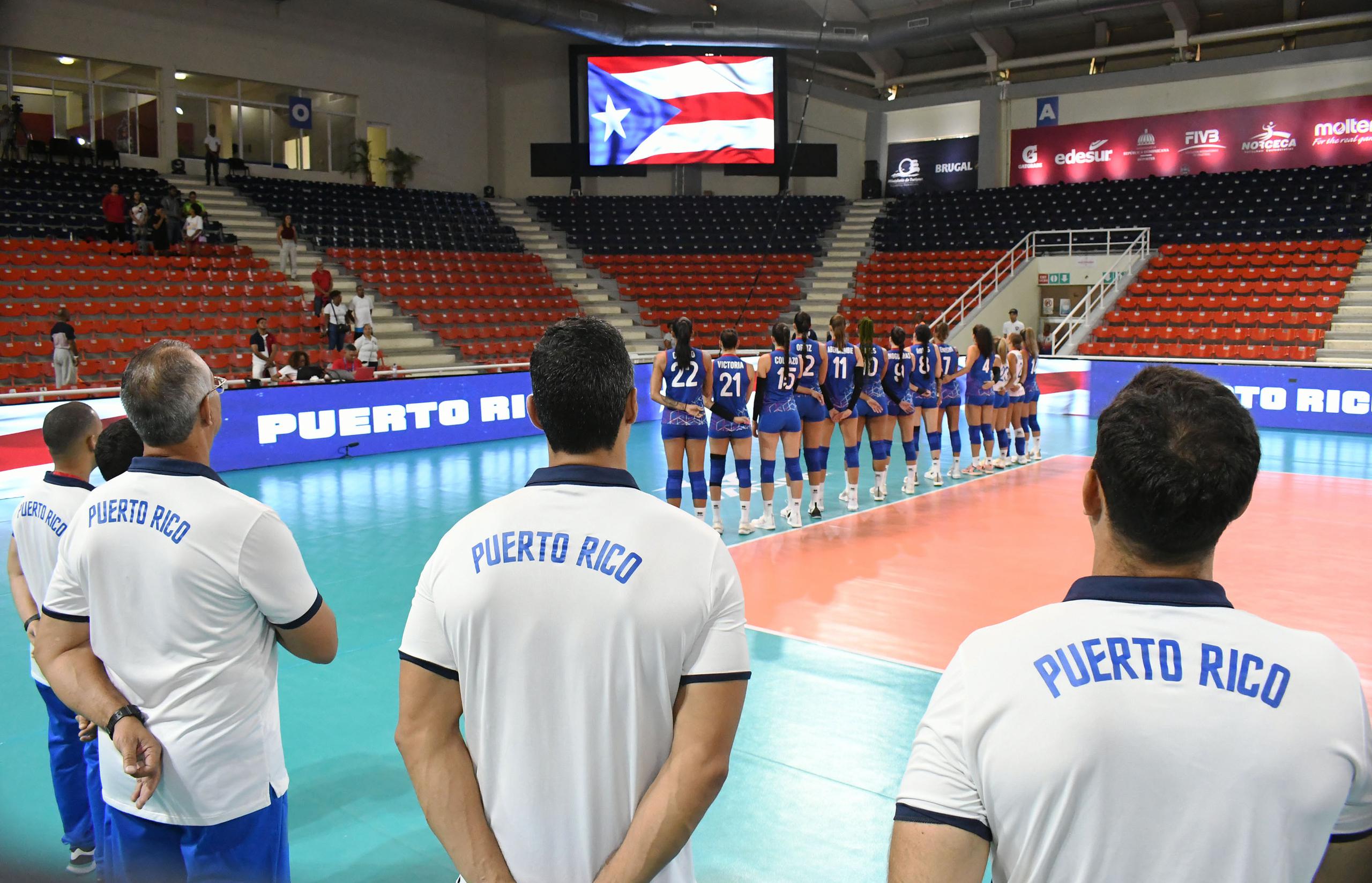 El cuerpo técnico en primer plano y las jugadora al fondo siguen el protocolo del himno nacional previo al juego ante Canadá.