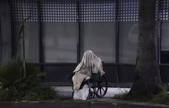 Una persona desamparada está sentada en una silla de ruedas bajo la lluvia en Sunset Blvd., en el barrio de Echo Park en Los Ángeles