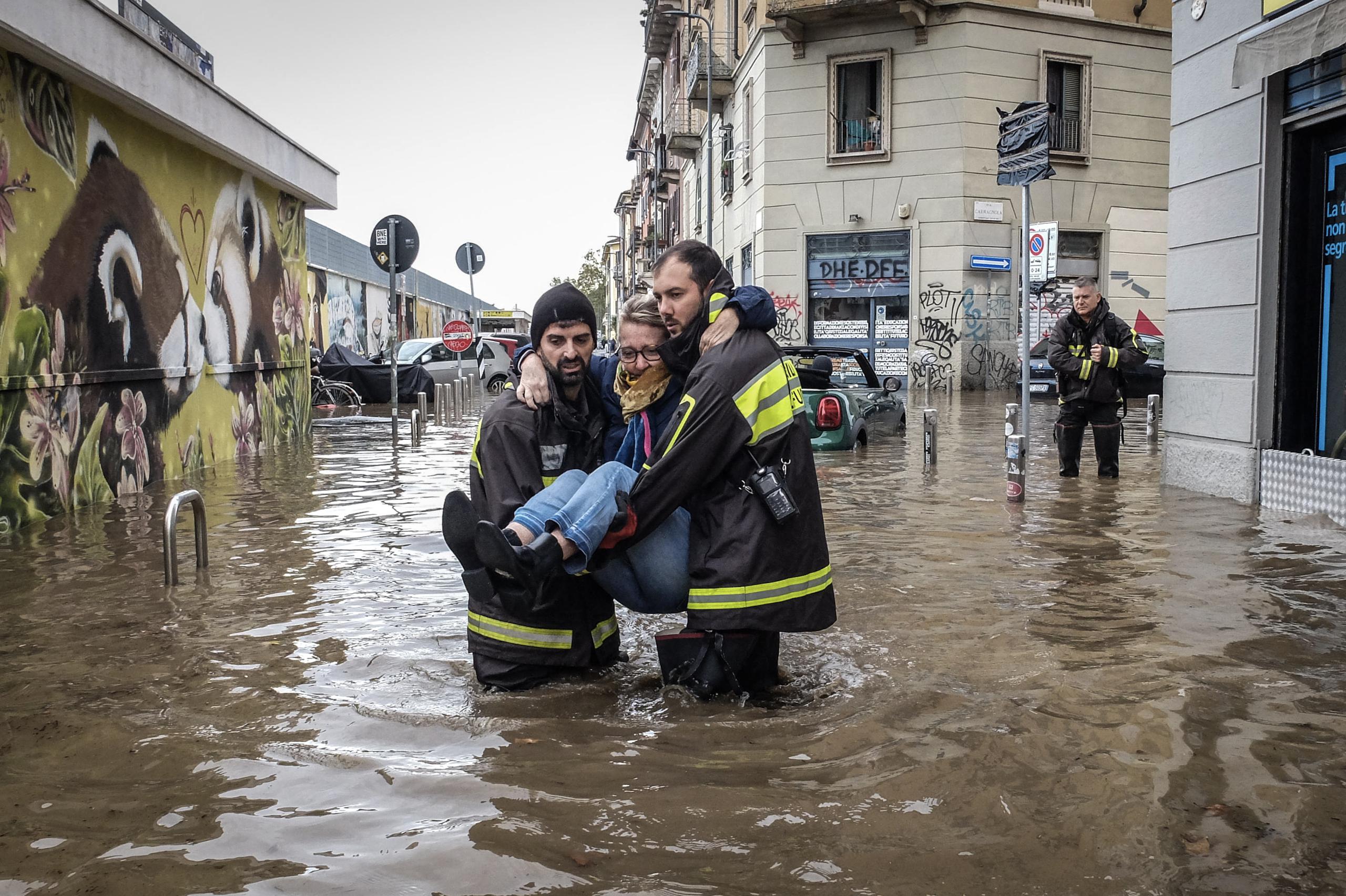 Los trabajadores de emergencia llevan a una mujer en medio de inundaciones en una calle, después de que una tormenta causó el desbordamiento del río Seveso, en el distrito de Isola, en Milán, Italia. EFE/MATTEO CORNER
