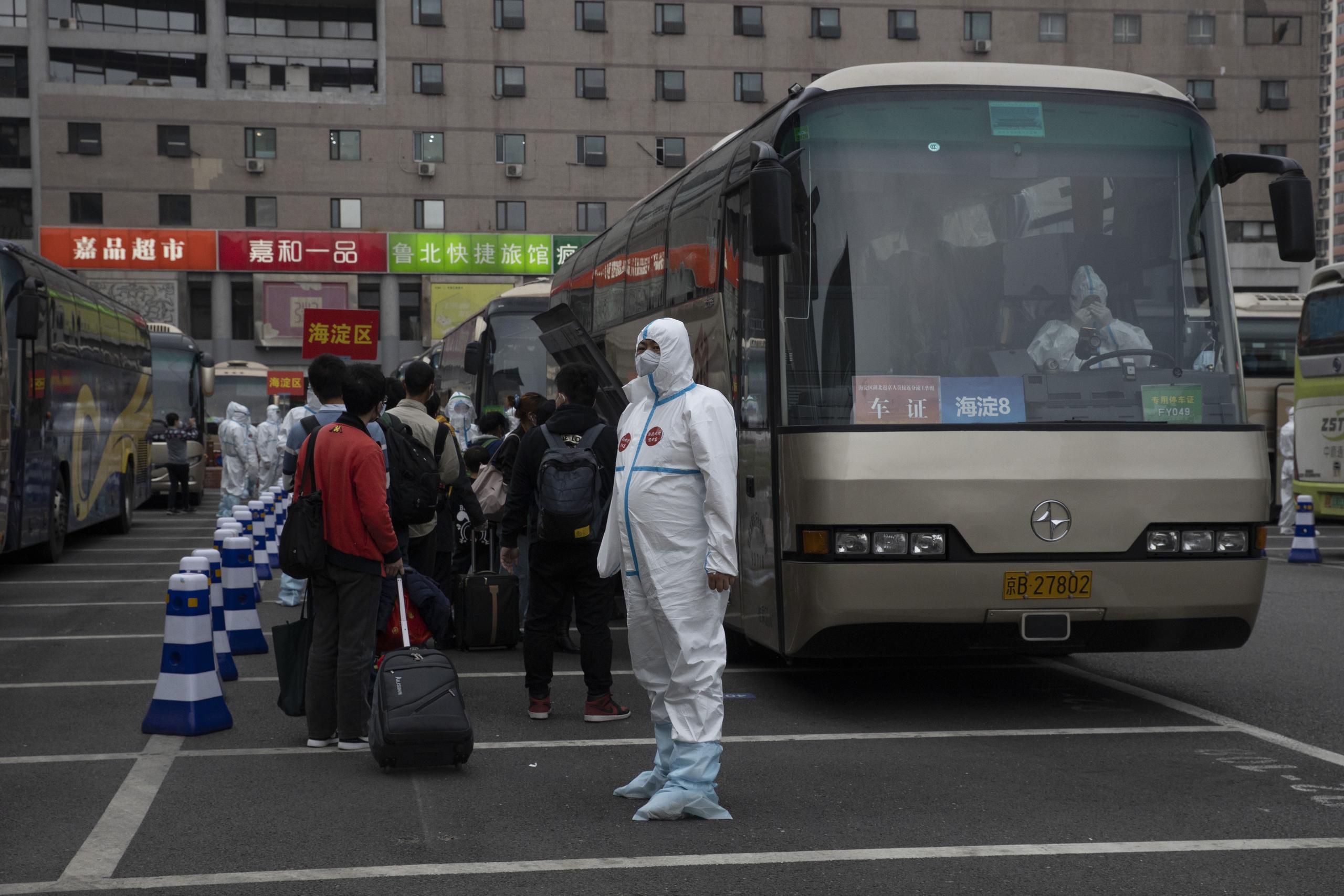 Un empleado con ropa protectora guía a pasajeros procedentes de Wuhan a abordar buses tras llegar en tren a Beijing.